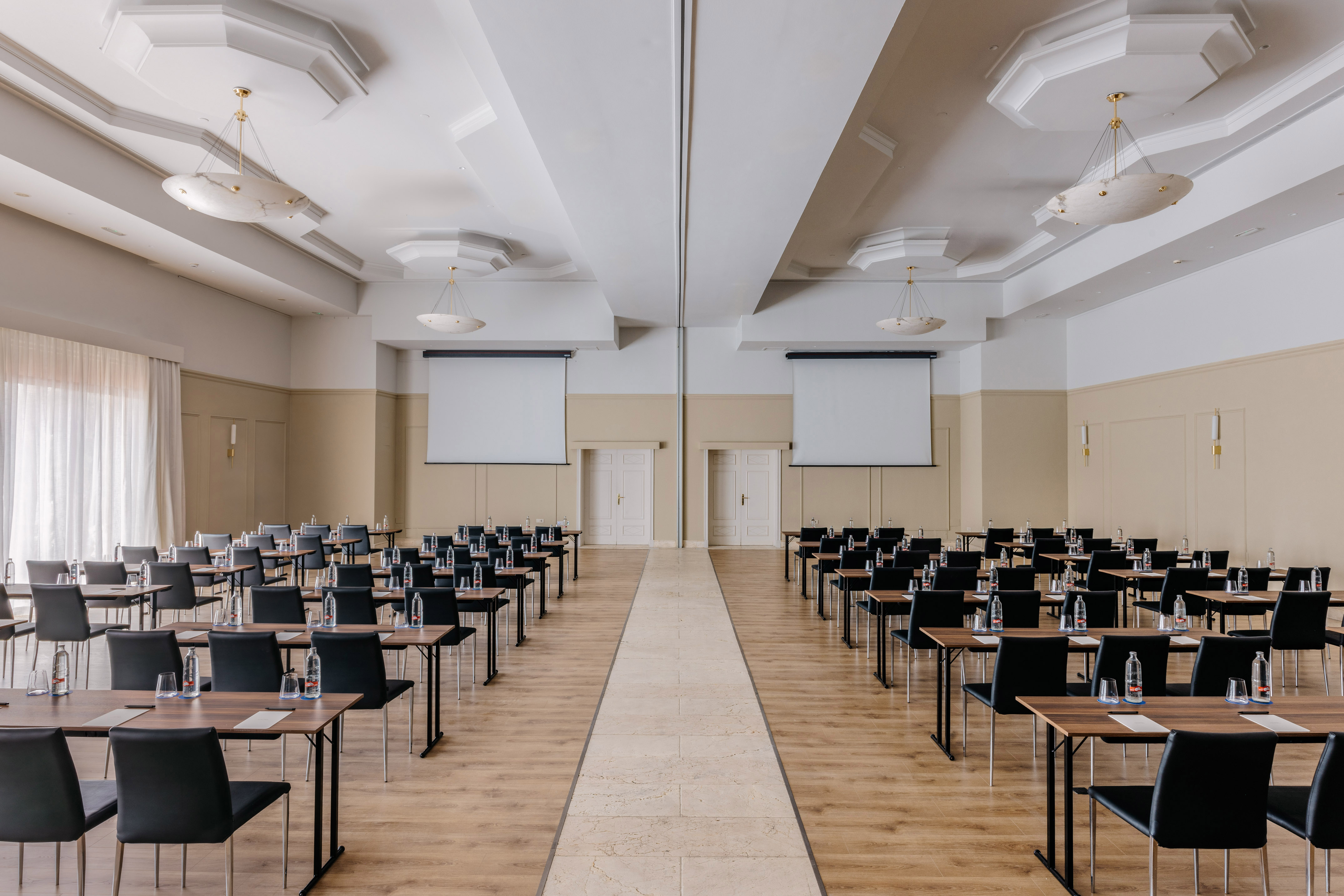 Empty conference room with tables, chairs, two screens, and central aisle.