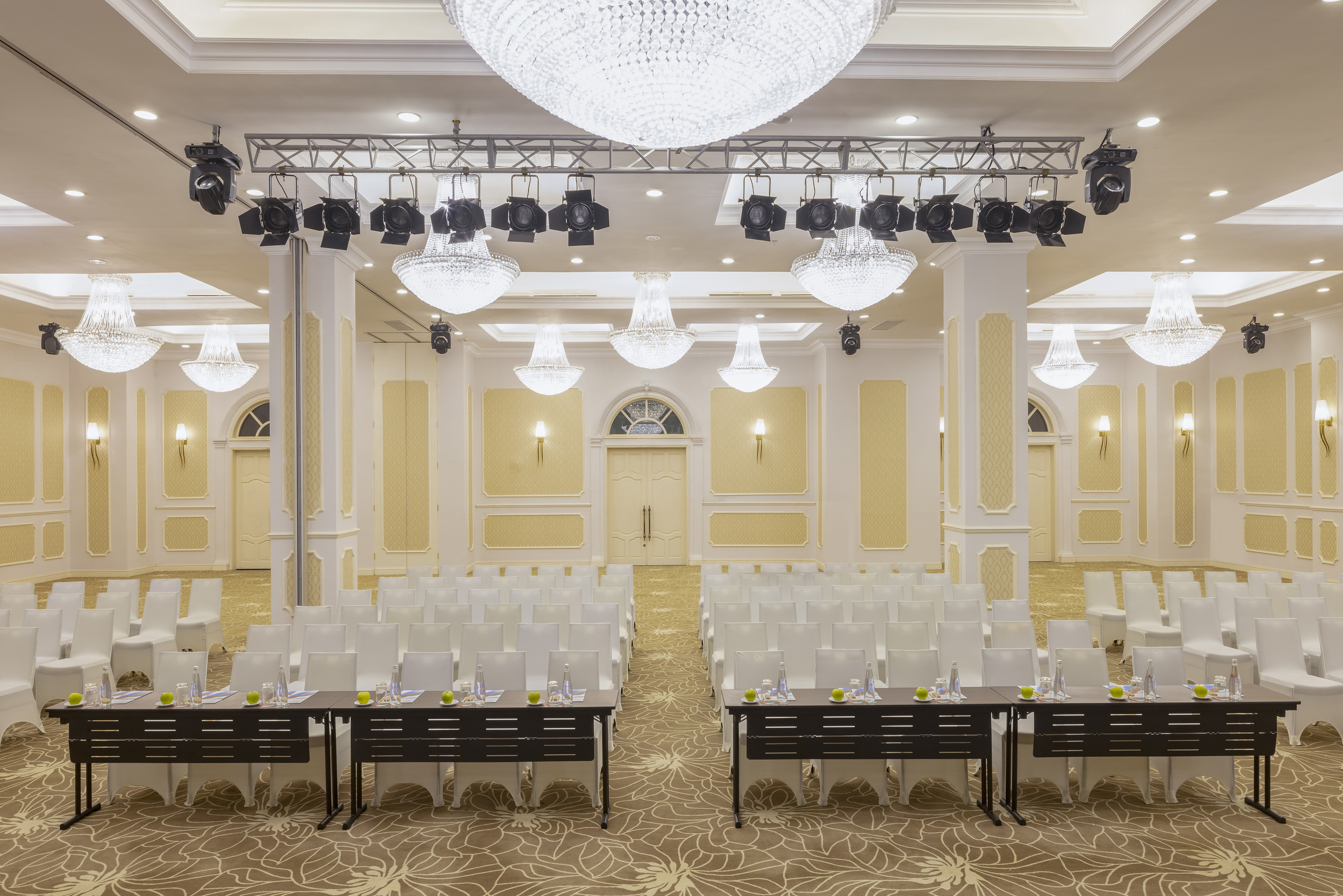 Elegant conference room with white chairs, chandeliers, and presentation tables.