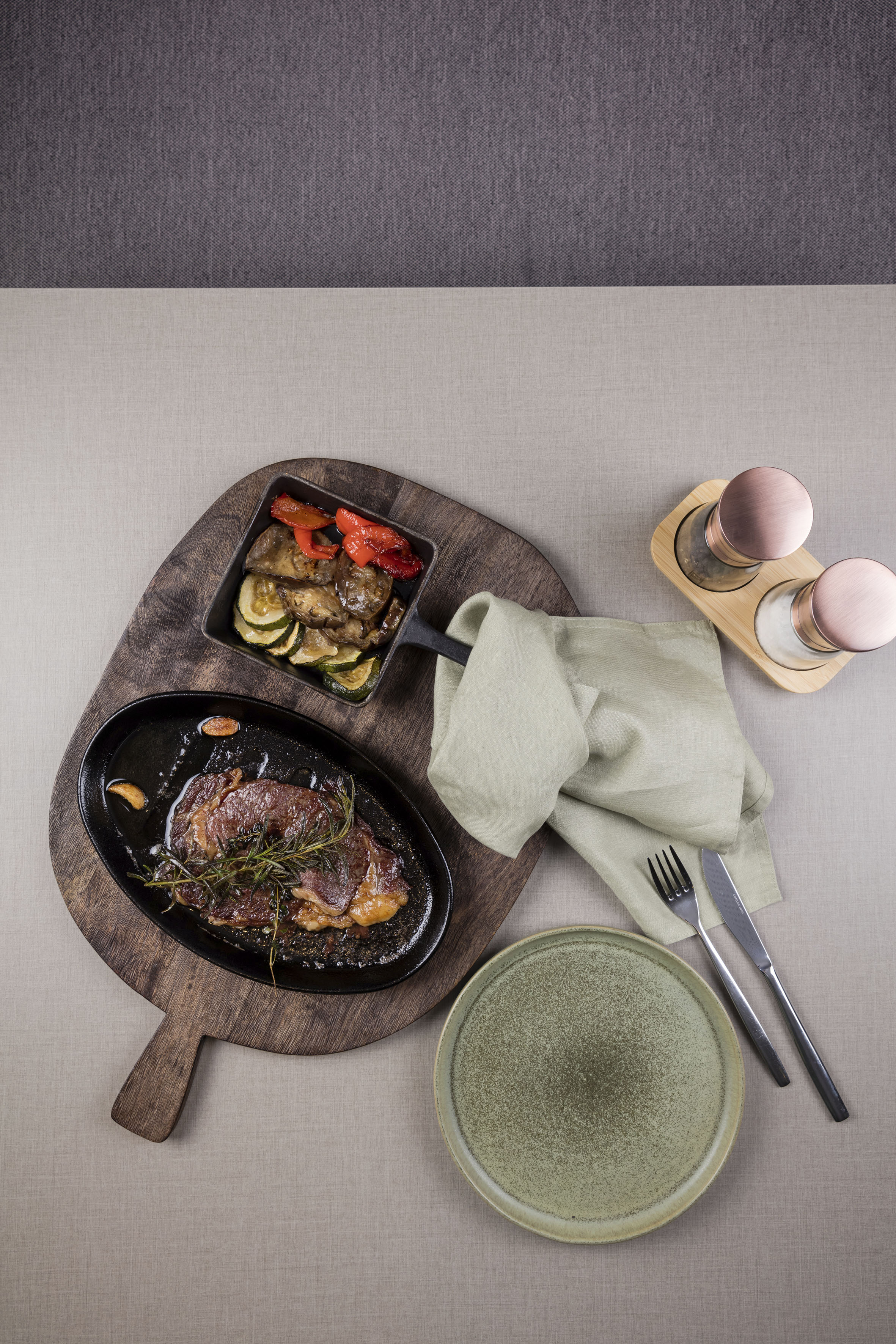 Pan-seared steak with rosemary, roasted vegetables, elegant meal setting.