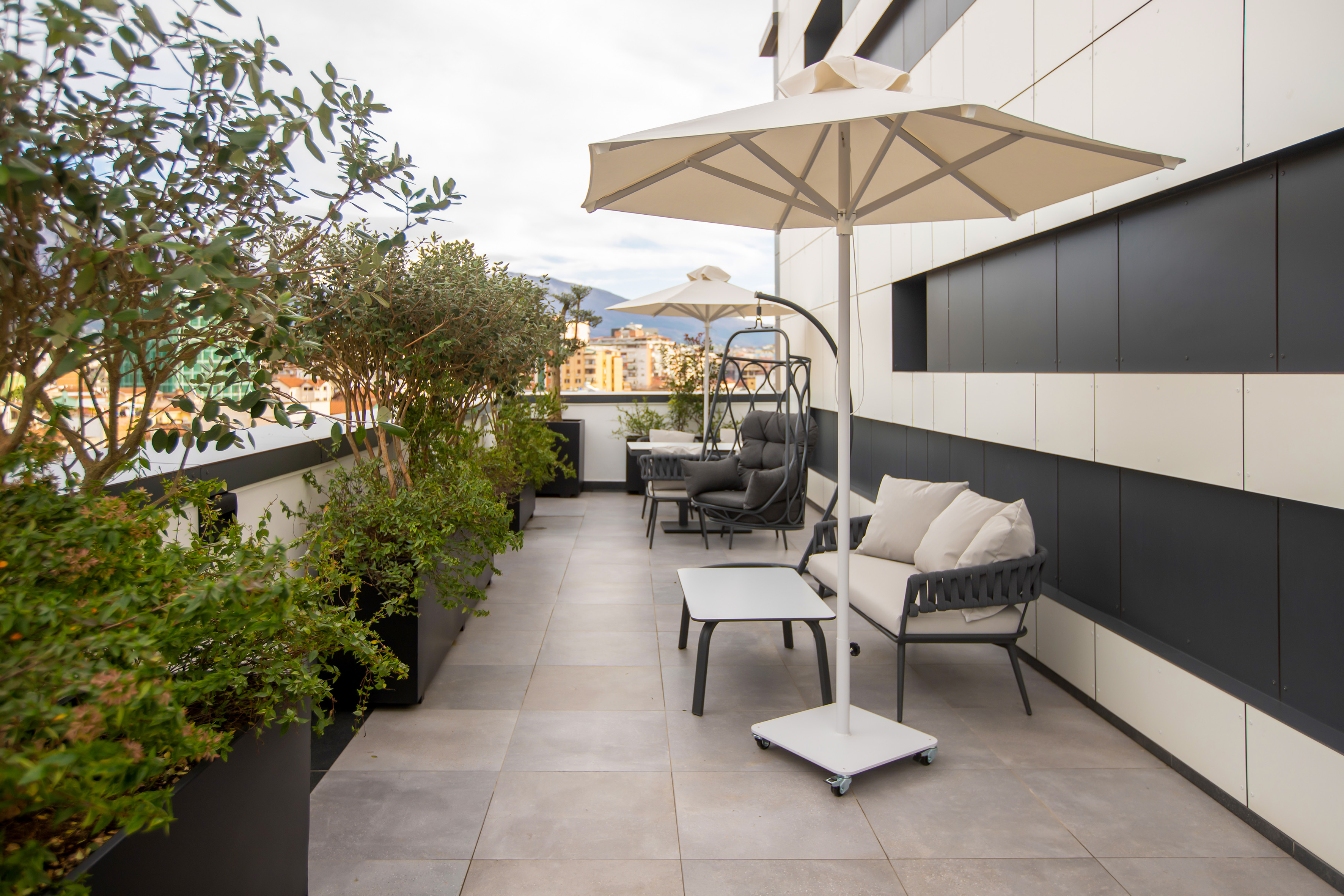 Modern rooftop terrace with outdoor furniture, plants, umbrellas, and city view.