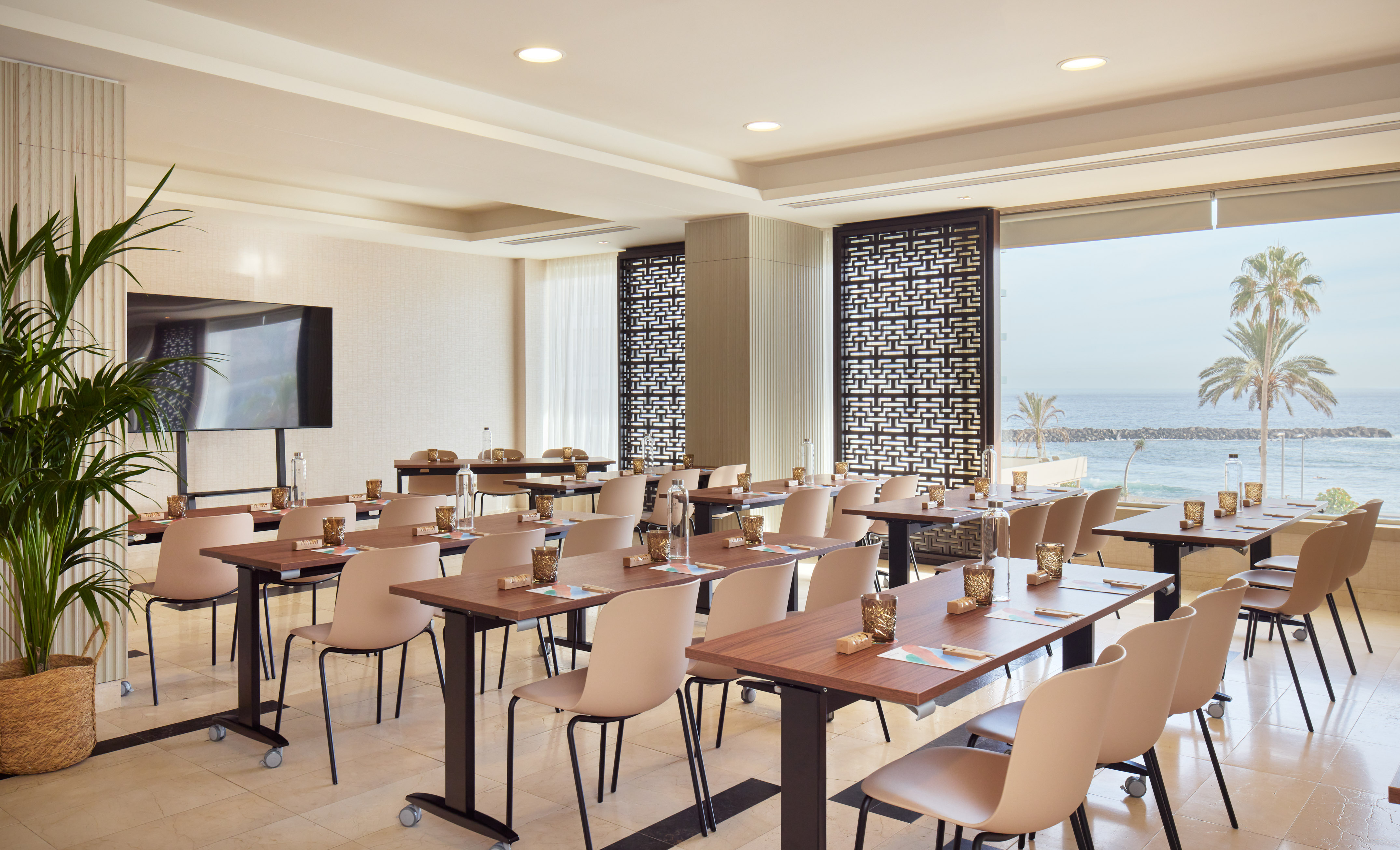 Bright conference room overlooking ocean, desks, and TV screen for presentations.
