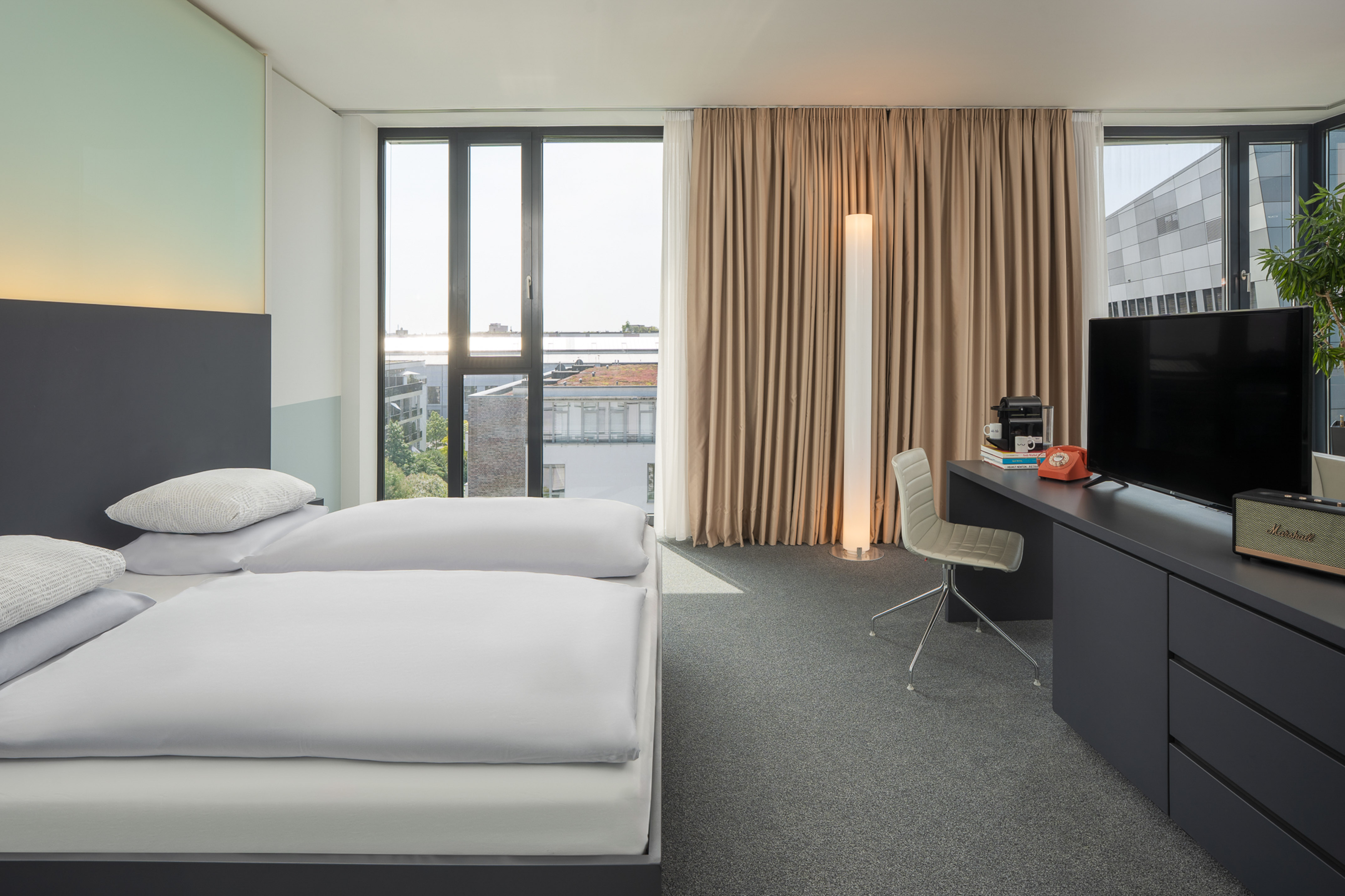 Modern hotel room with bed, desk, city view, and large windows.