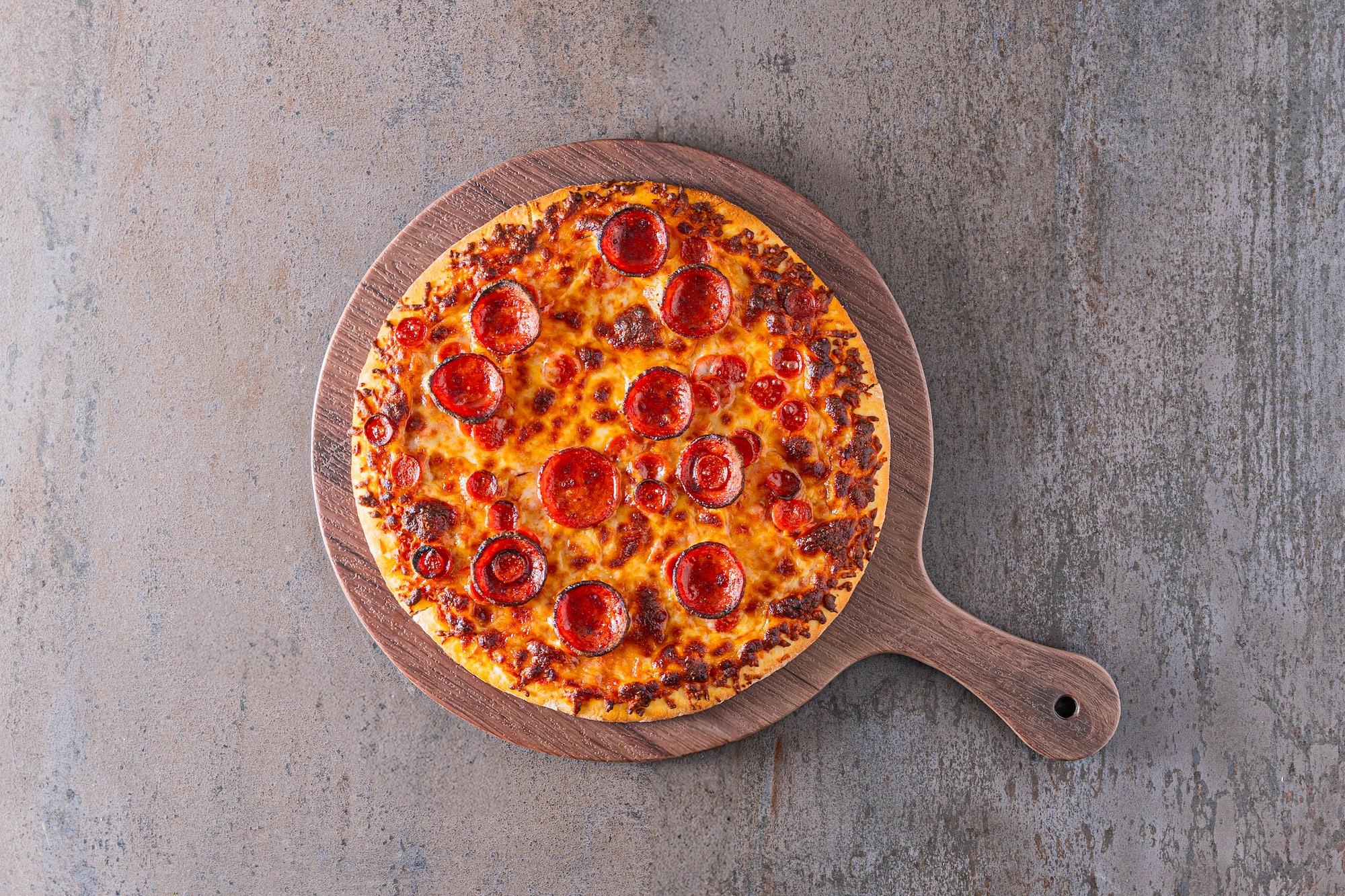 Round pepperoni pizza with crispy crust and melted cheese on a wooden board.