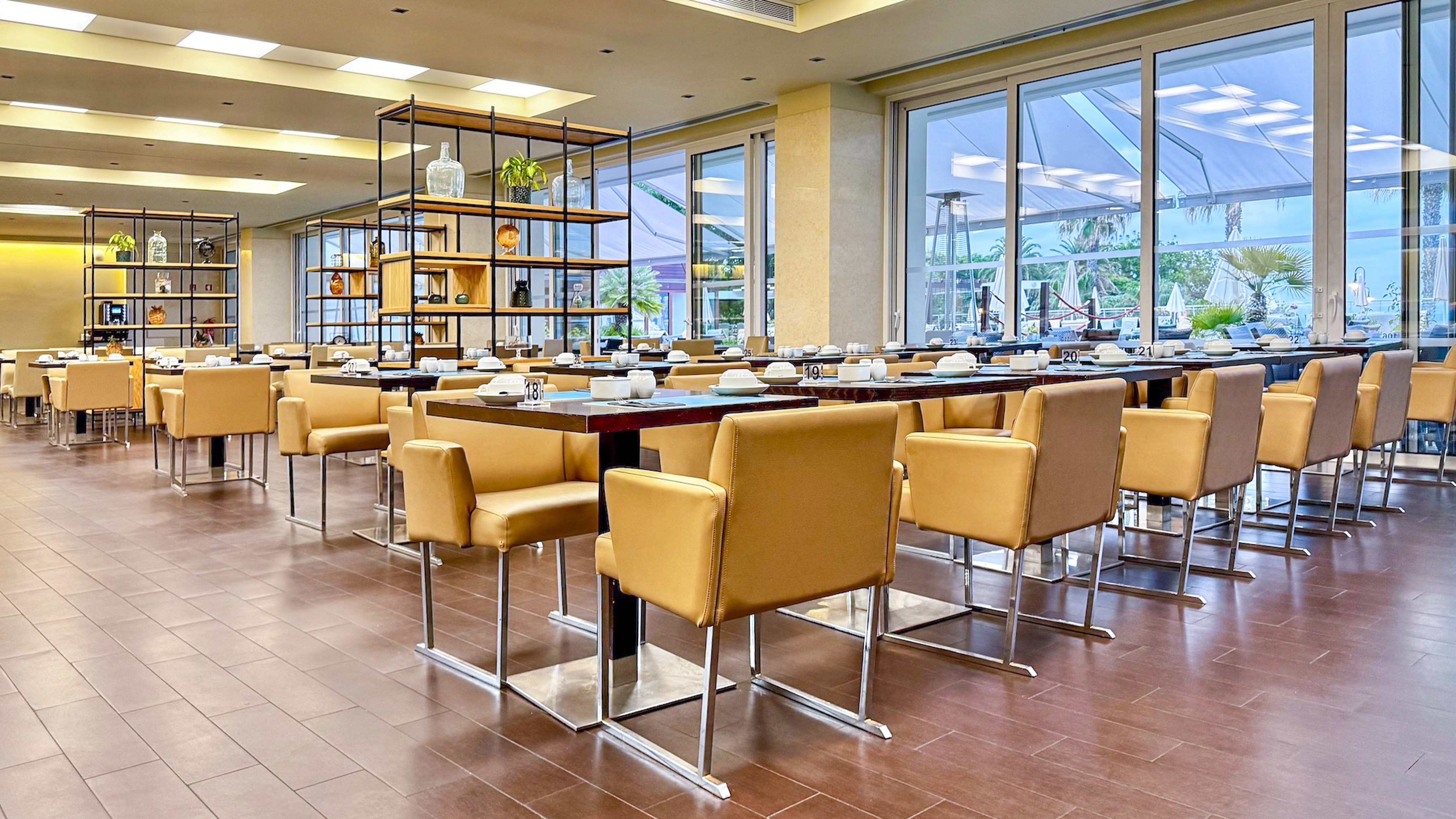 Modern restaurant dining room with yellow chairs, dark tables, and large windows.