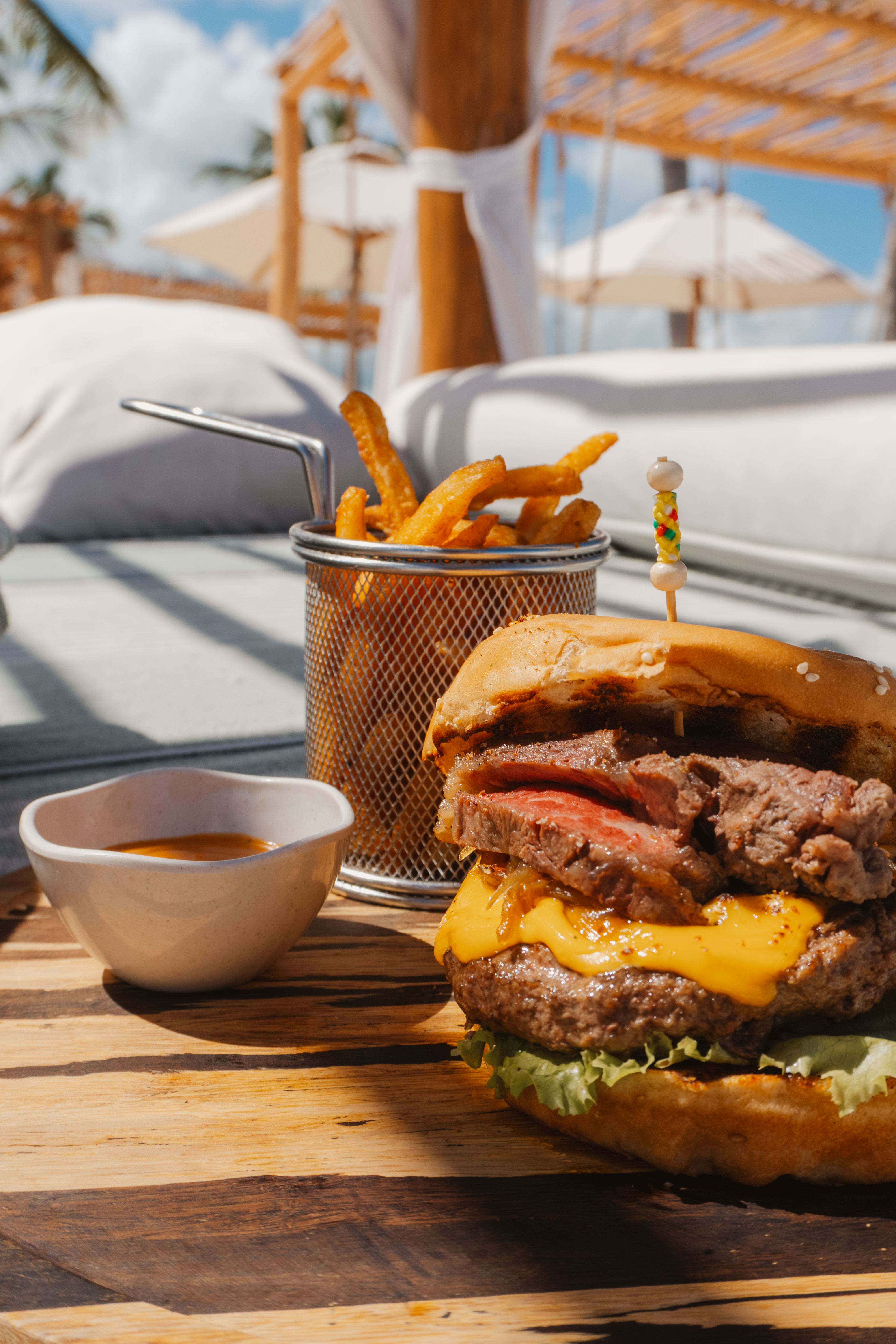 Gourmet steak burger, fries, and sauce on wood, outdoor resort.