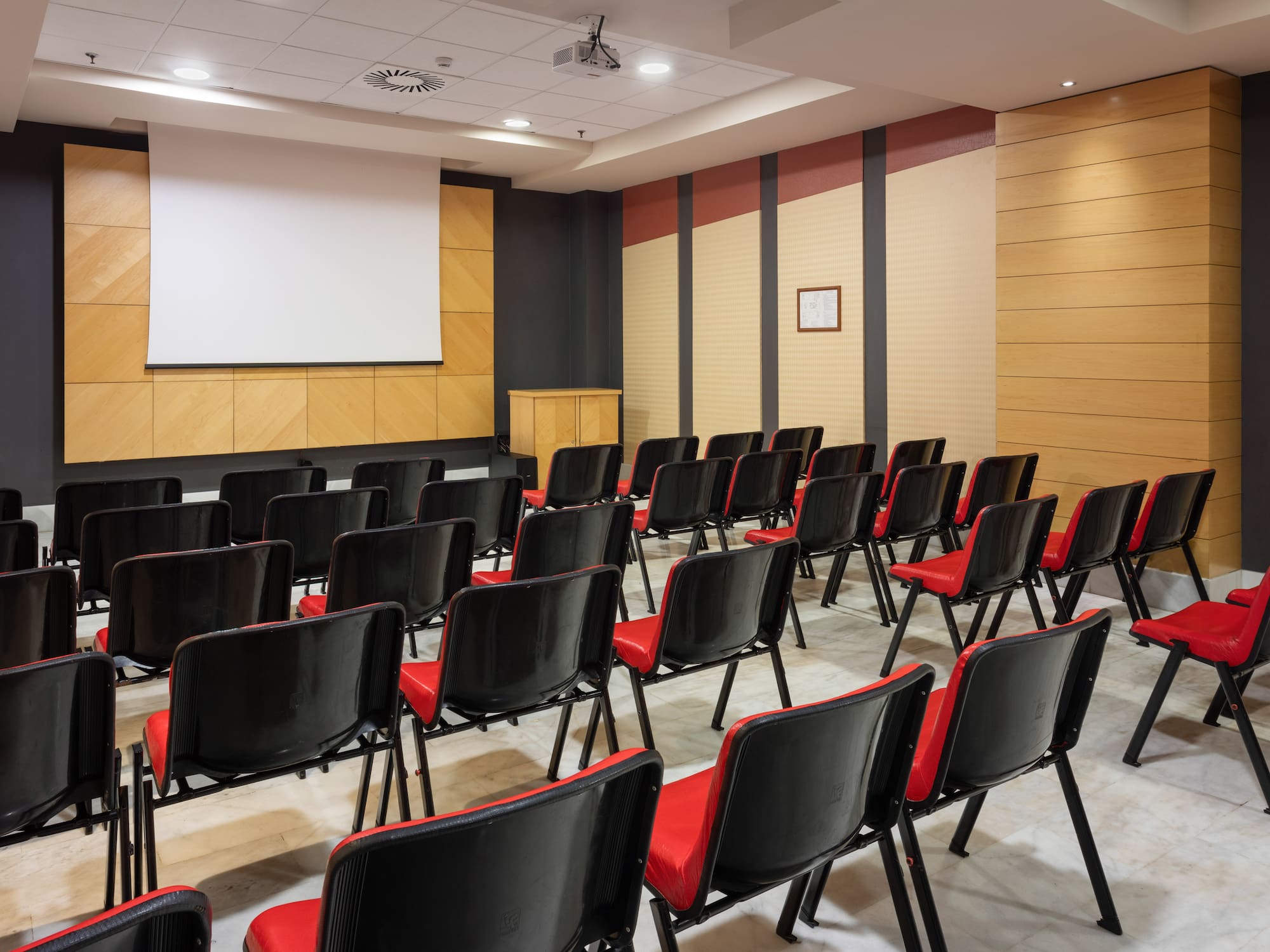 Empty modern conference room with projector screen and rows of red chairs.