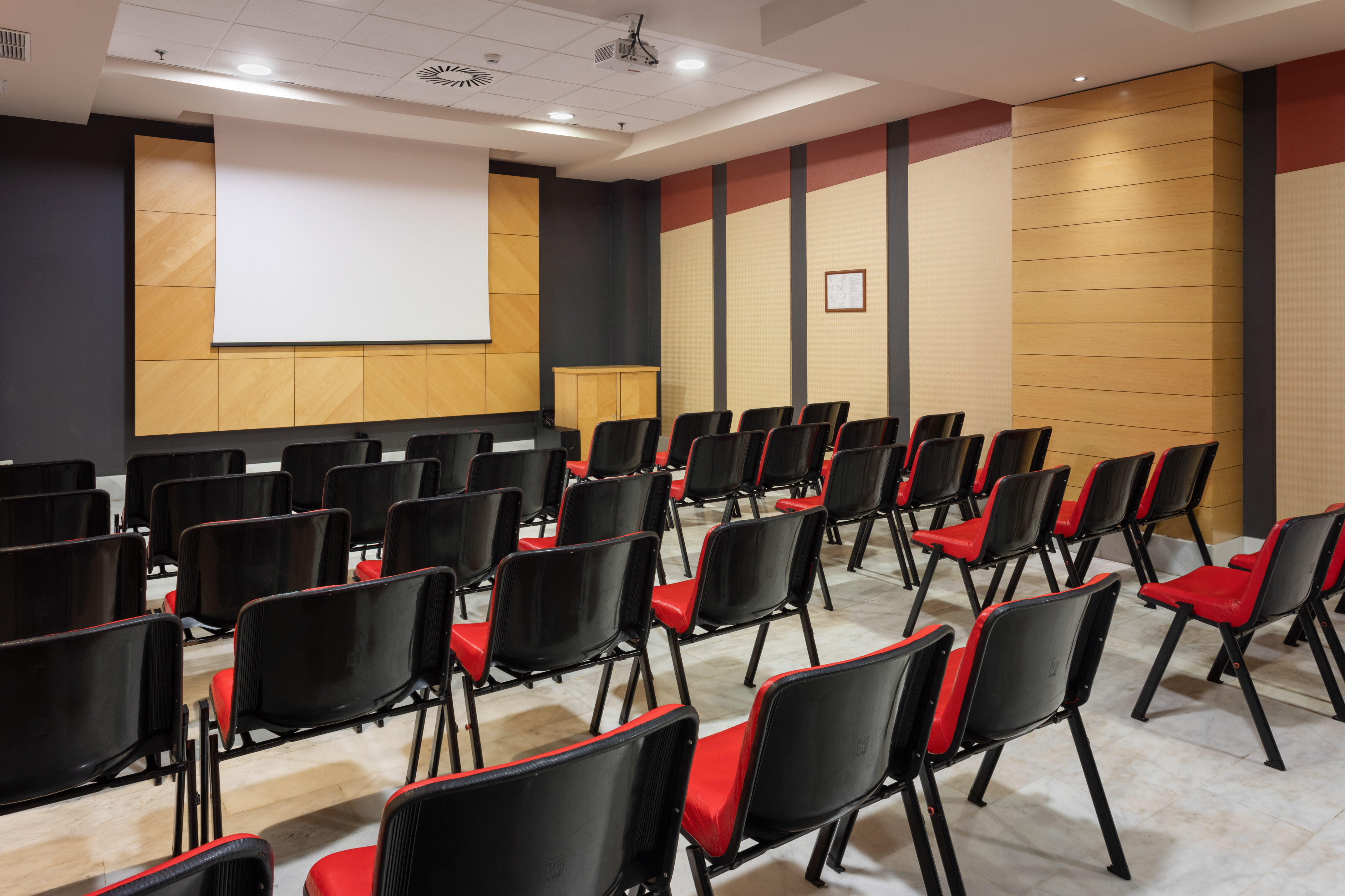 Empty modern conference room with projector screen and rows of red chairs.