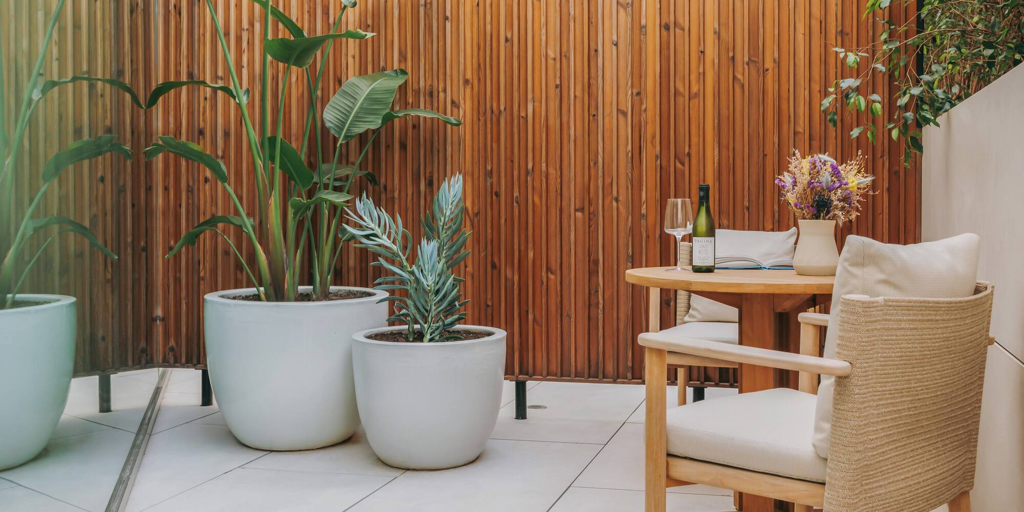 Patio with wood screen, large potted plants, outdoor dining table and wine.
