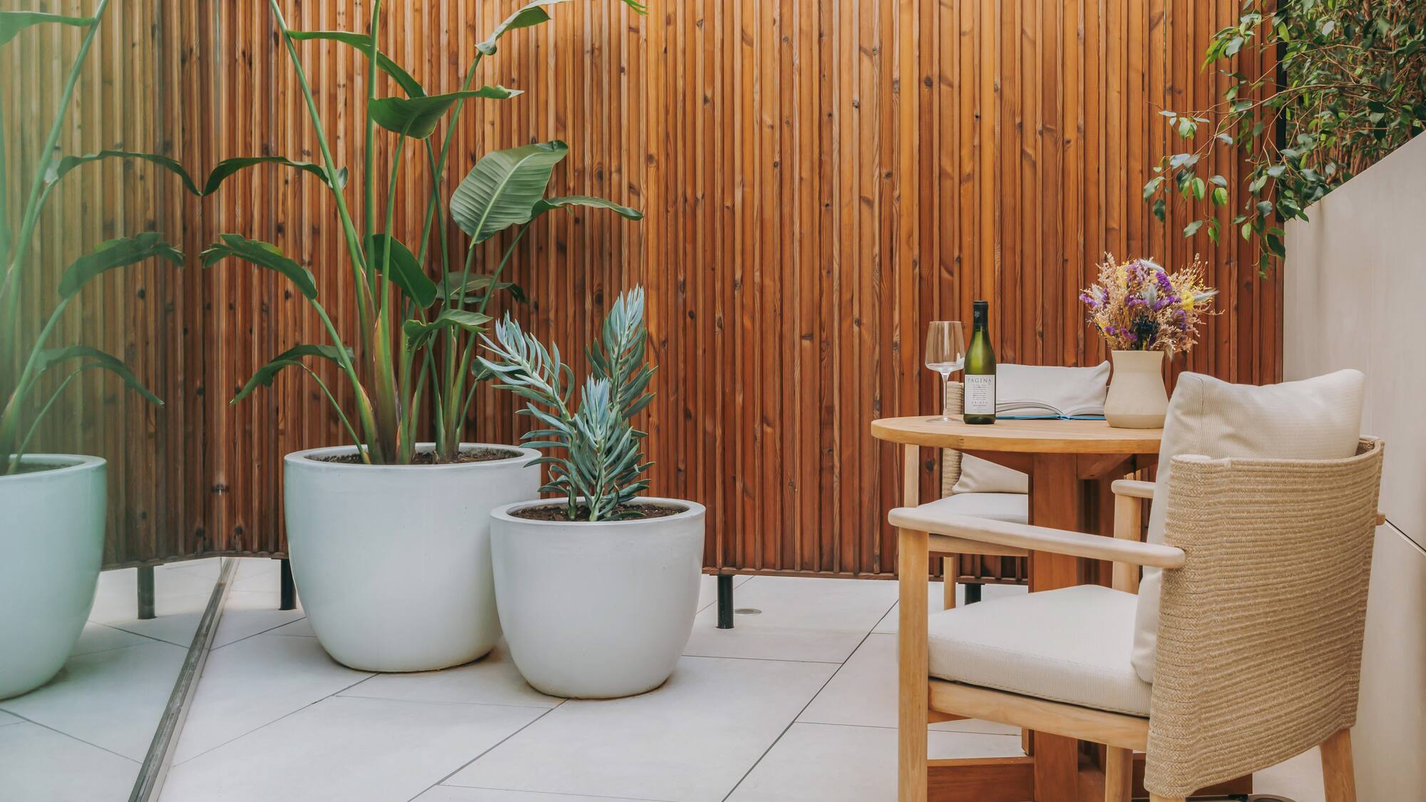 Patio with wood screen, large potted plants, outdoor dining table and wine.
