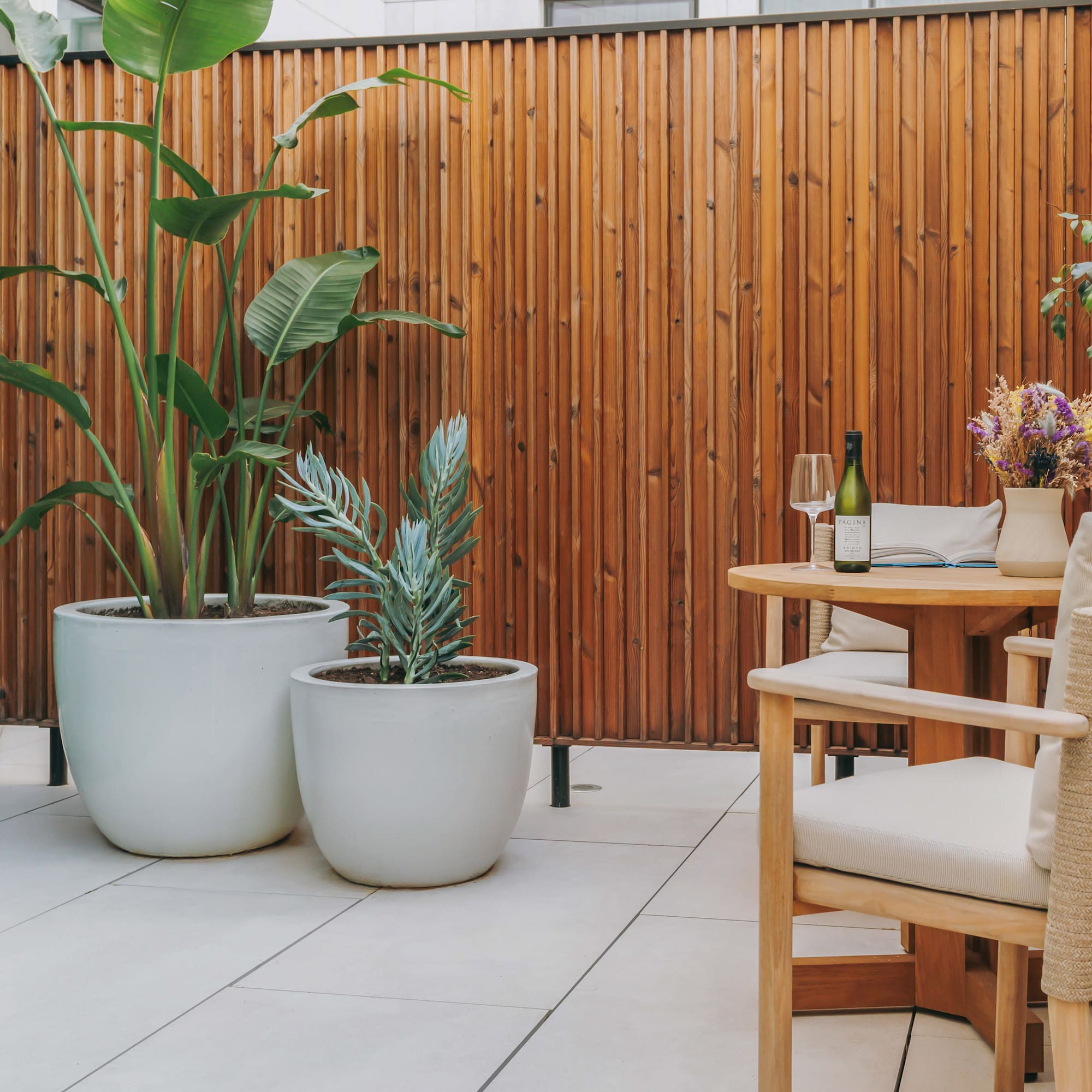 Patio with wood screen, large potted plants, outdoor dining table and wine.