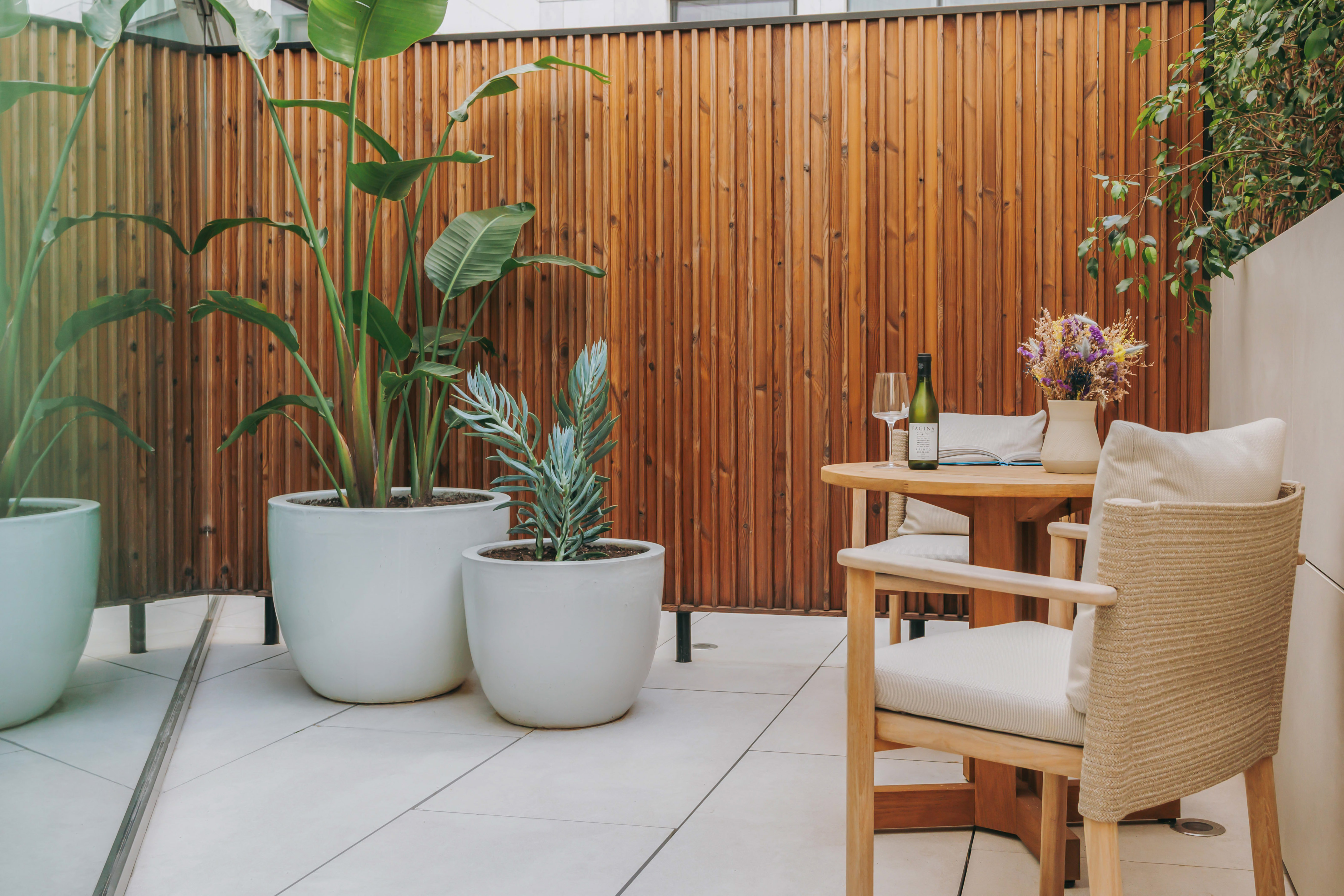 Patio with wood screen, large potted plants, outdoor dining table and wine.