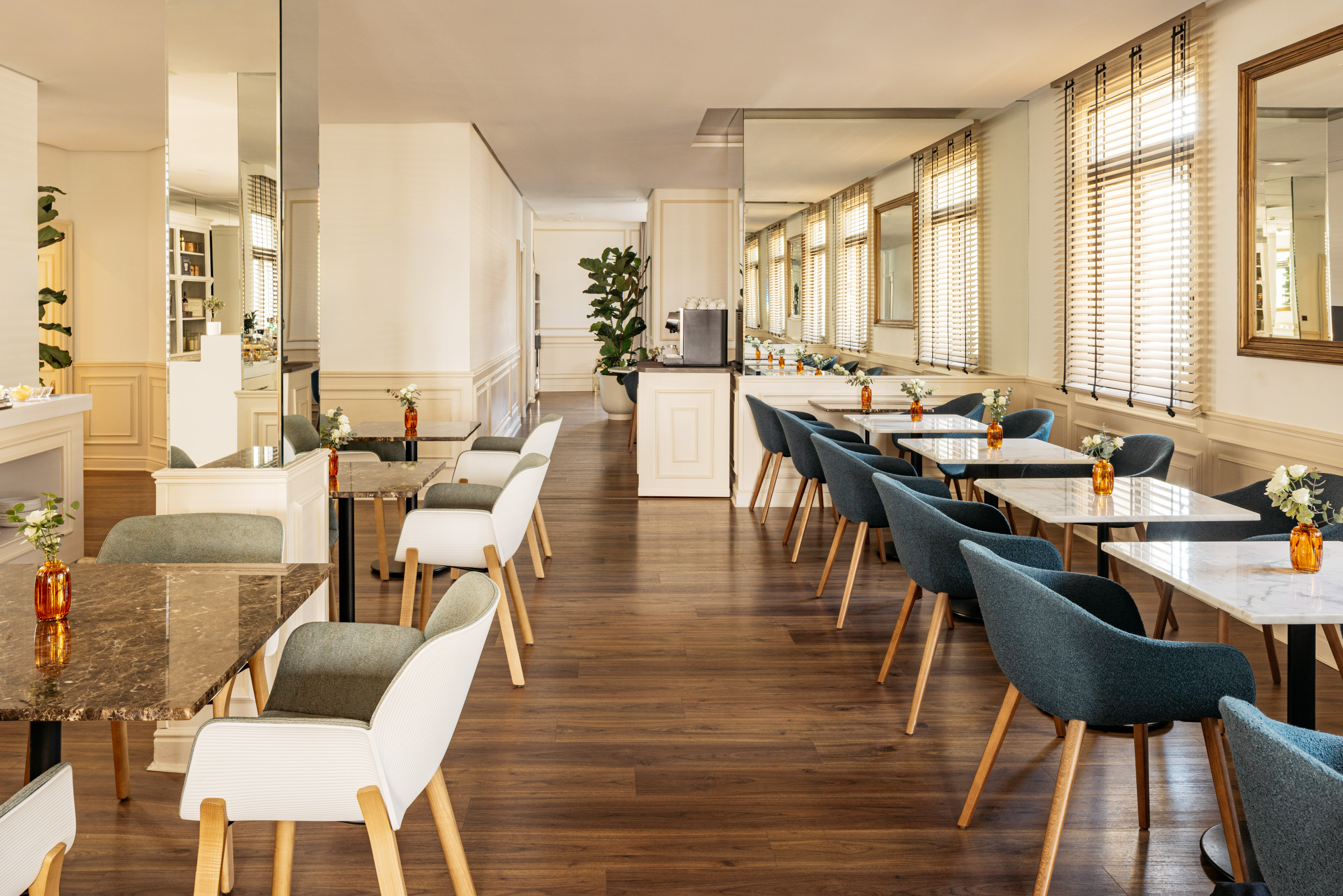 Modern restaurant dining room with teal & white chairs, marble tables, wood floors.