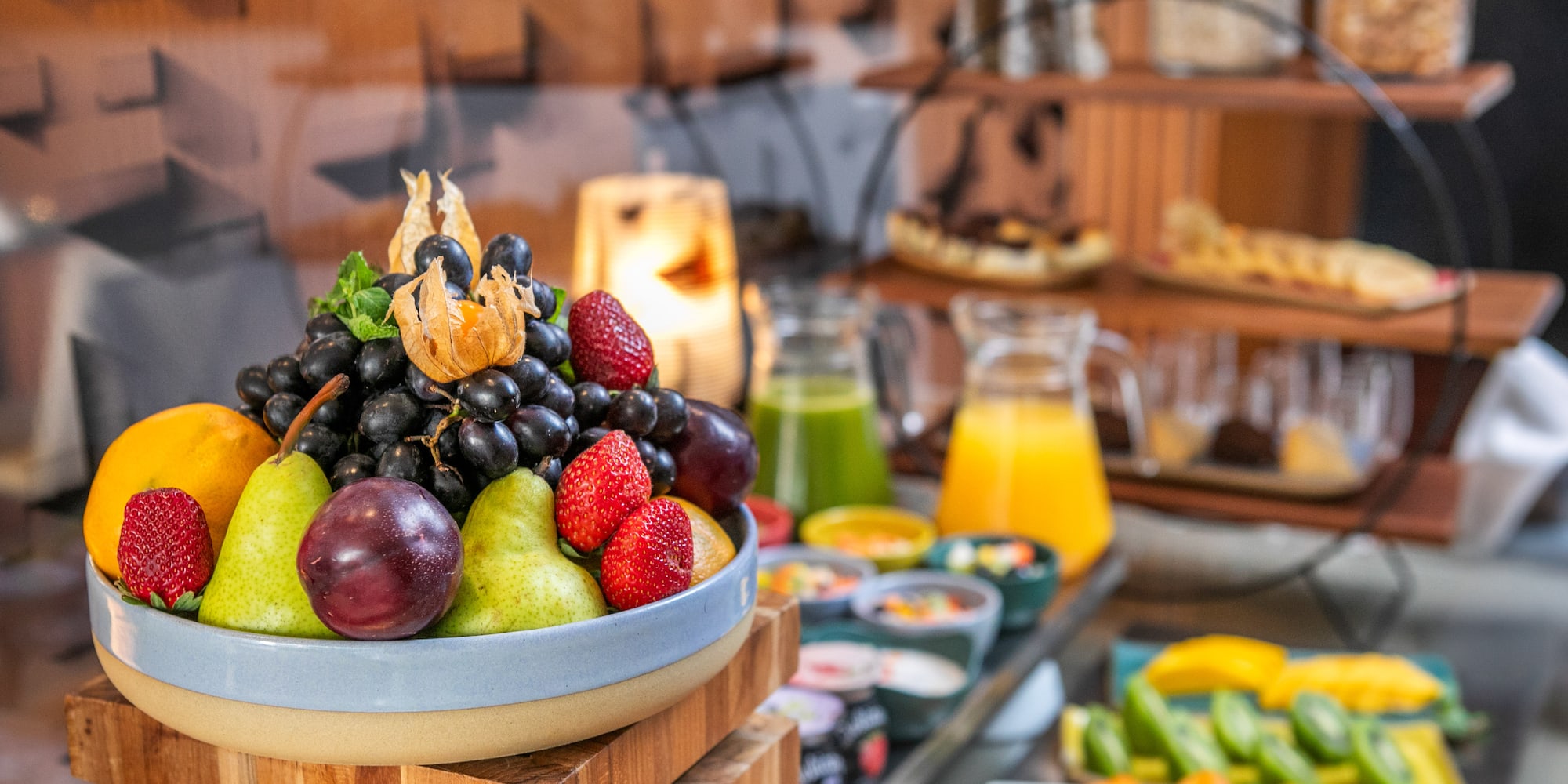 Fresh fruit, grapes, strawberries, pears, and juices at a hotel breakfast buffet.