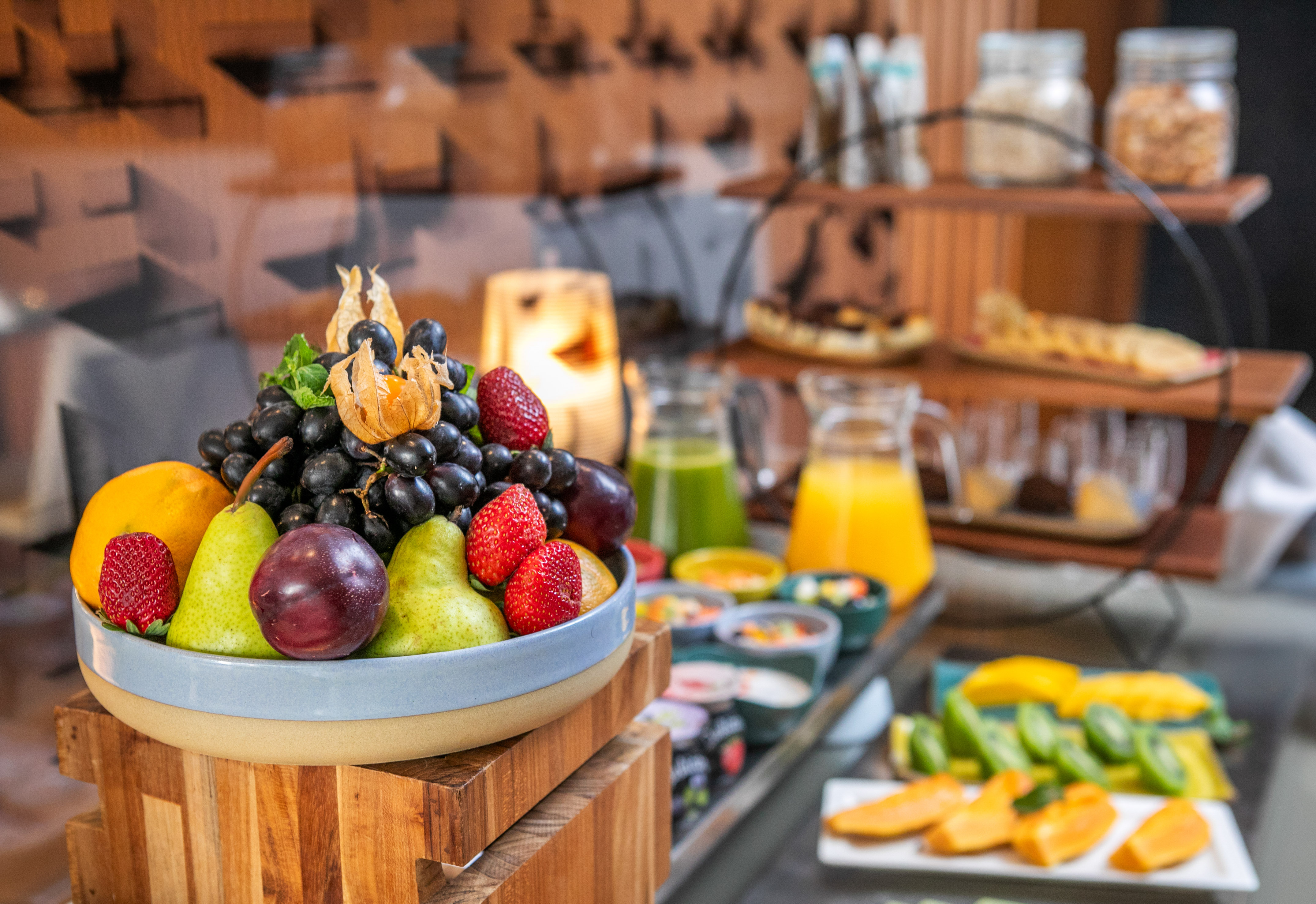 Fresh fruit, grapes, strawberries, pears, and juices at a hotel breakfast buffet.