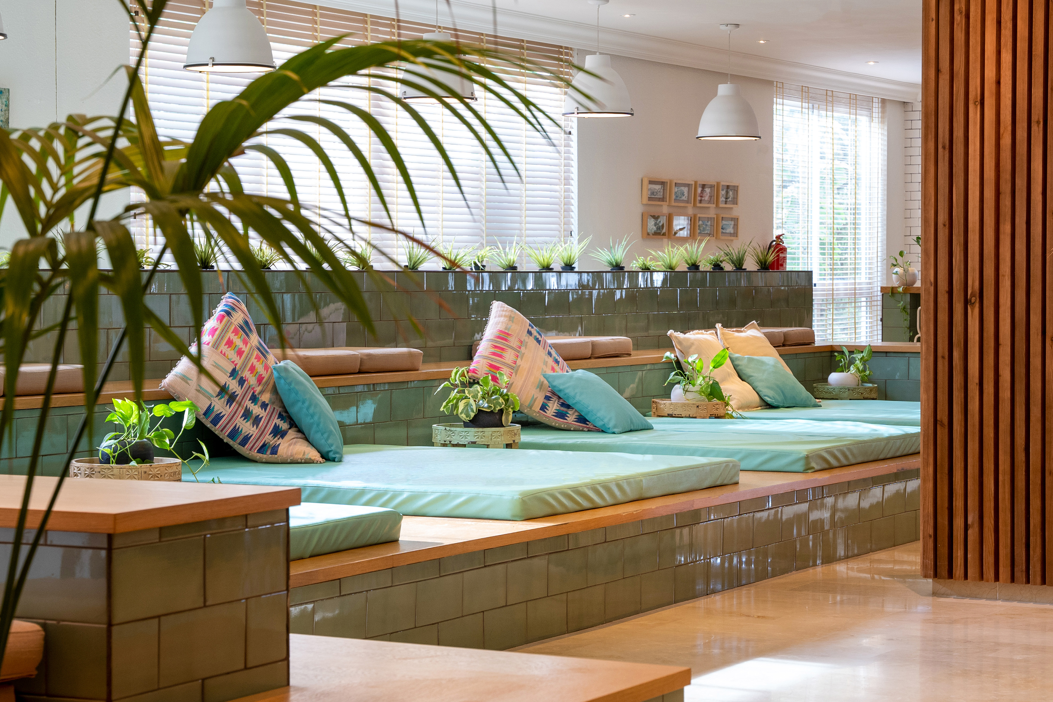 Modern lounge with green tiled seating, mint cushions, and potted plants.