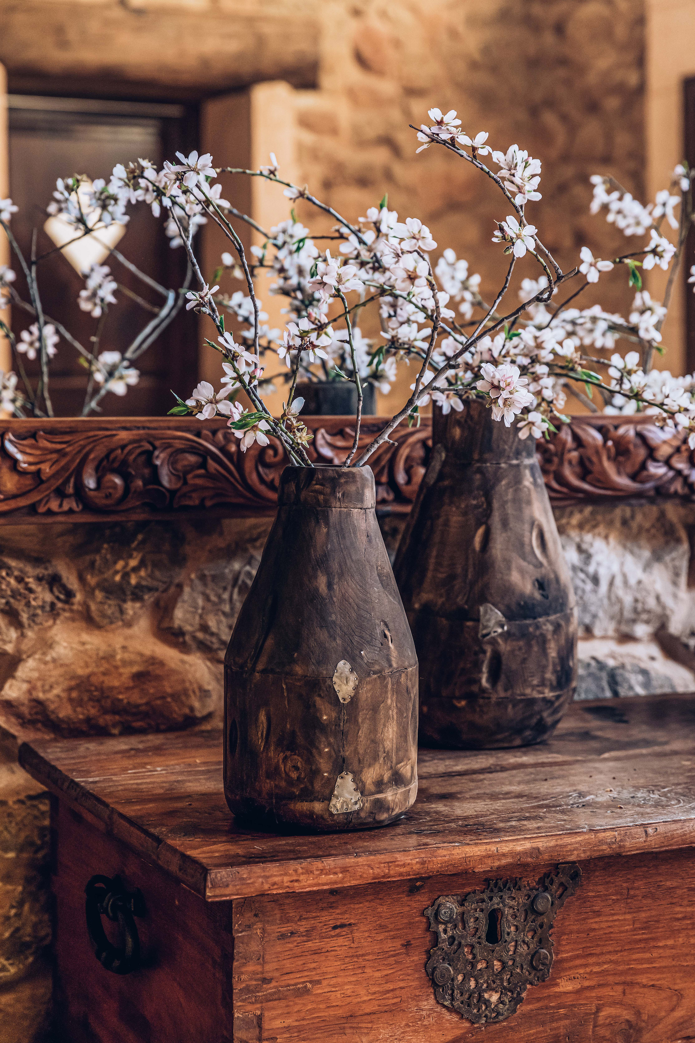 Almond blossoms in rustic wooden vases on antique carved chest.