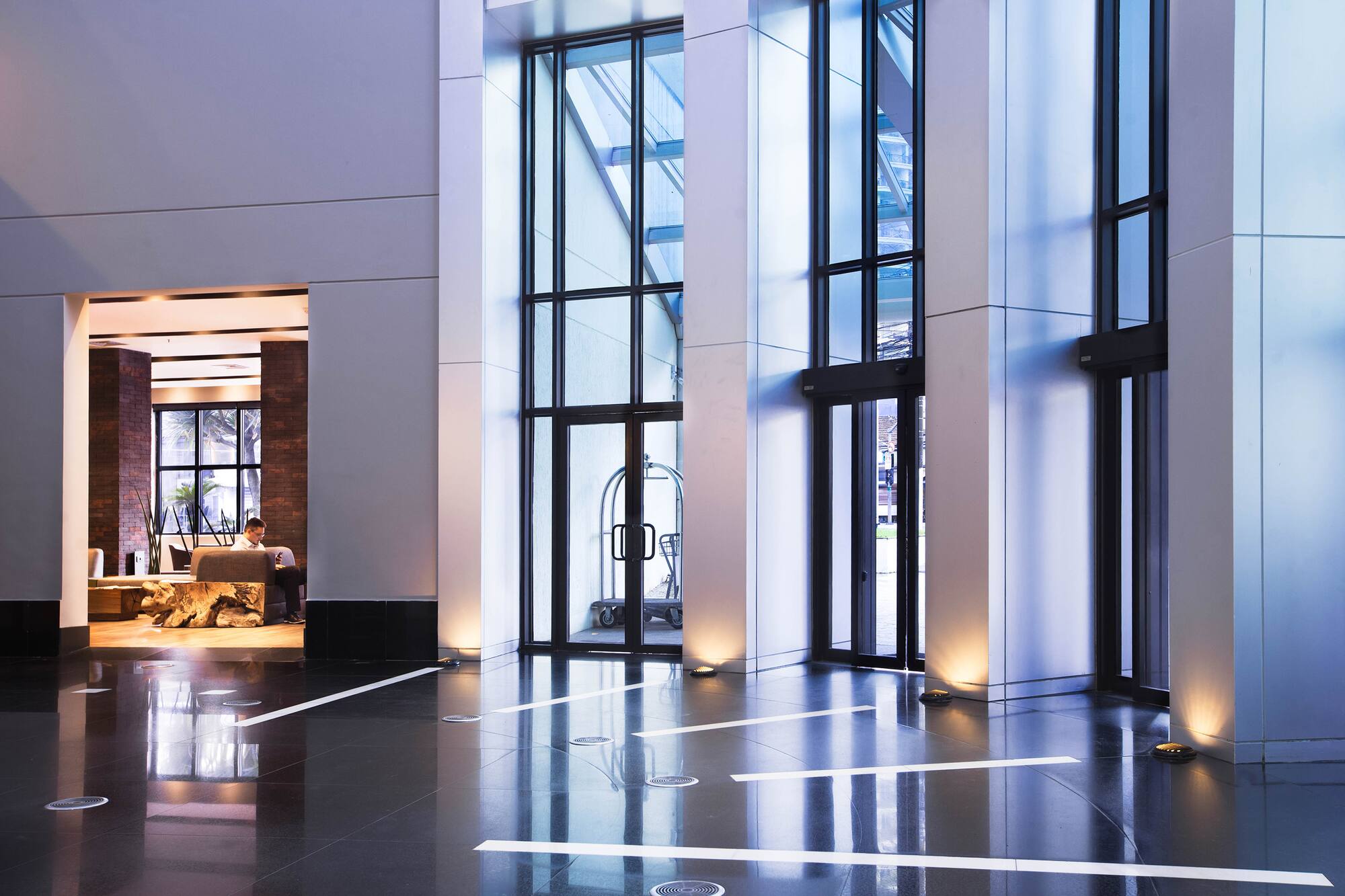 Modern hotel lobby with large glass doors, dark floor, and lounge area.