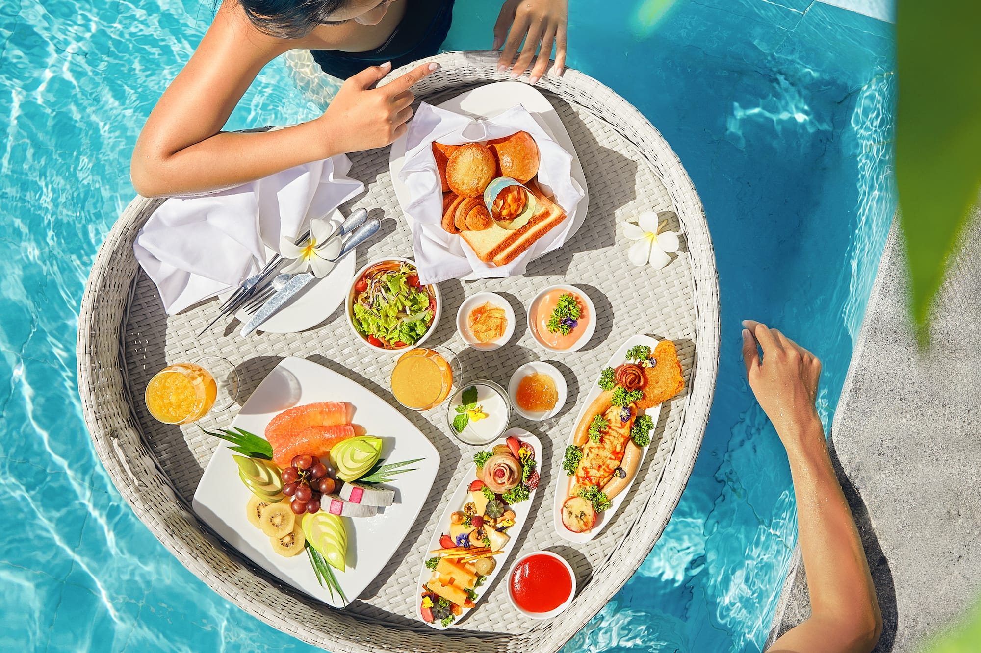 a man and woman in a pool with food on a tray