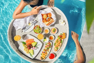 a man and woman in a pool with food on a tray