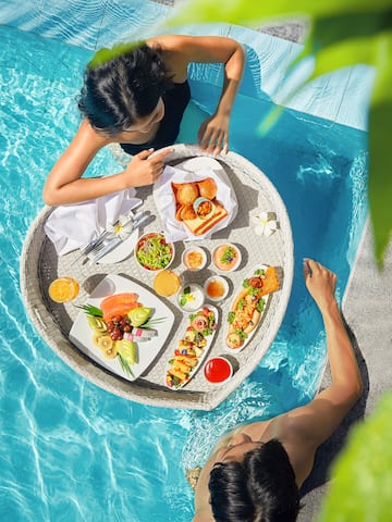 a man and woman in a pool with food on a tray