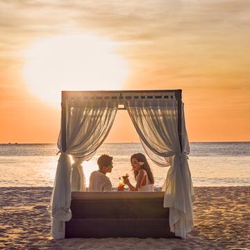 a couple sitting on a beach with a canopy over a body of water