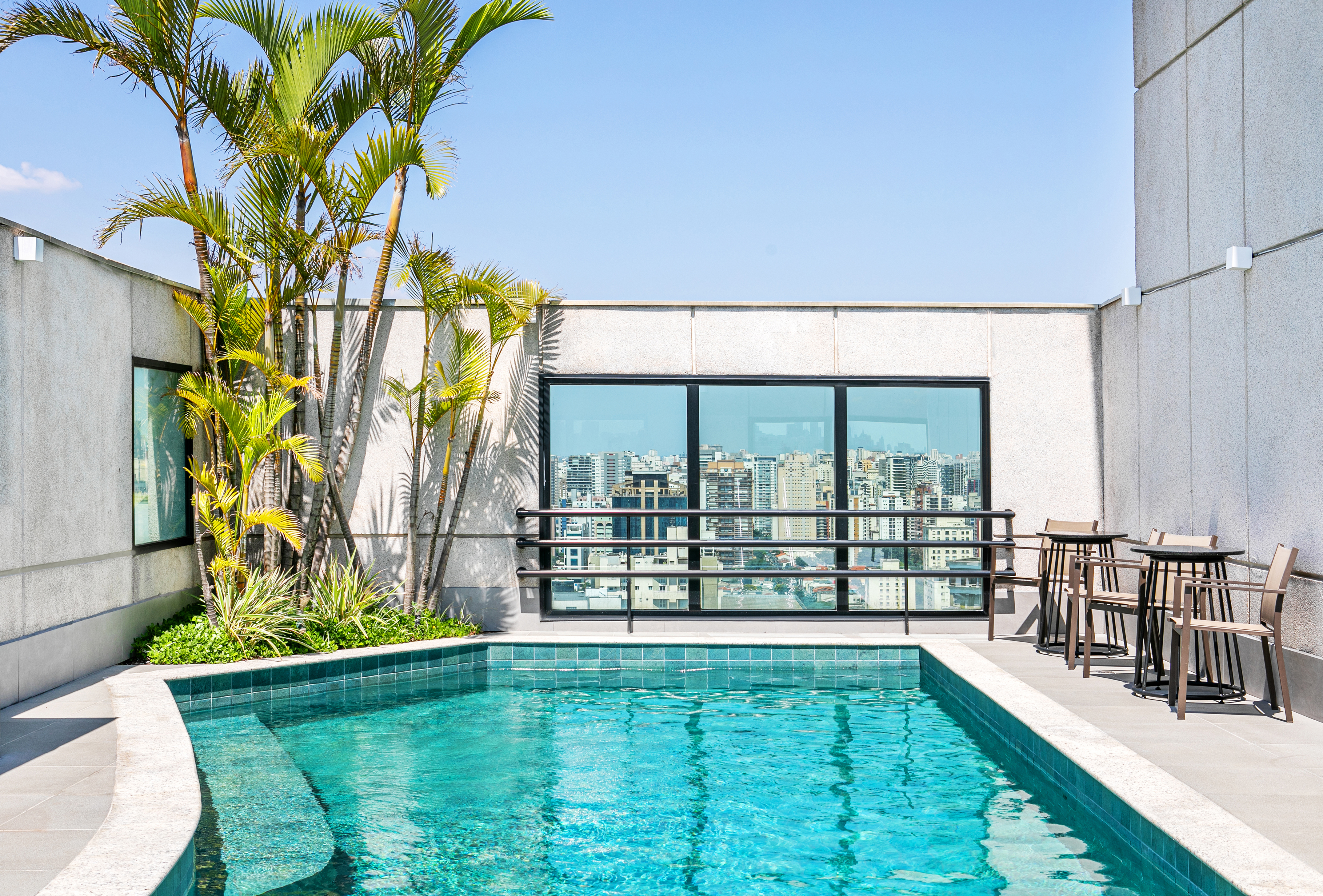 Rooftop pool, modern architecture, city skyline, palm trees, and outdoor seating.