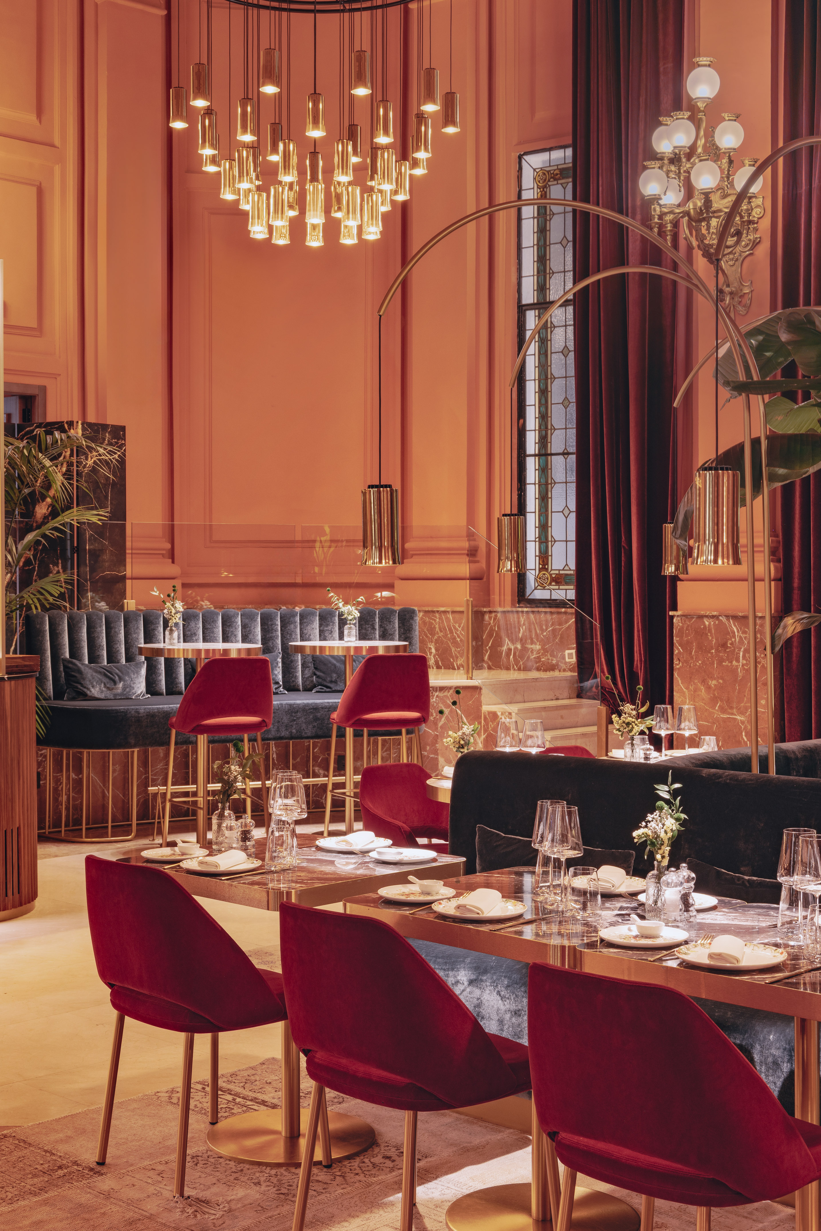 Luxury restaurant with peach walls, red velvet seating, and gold chandeliers.