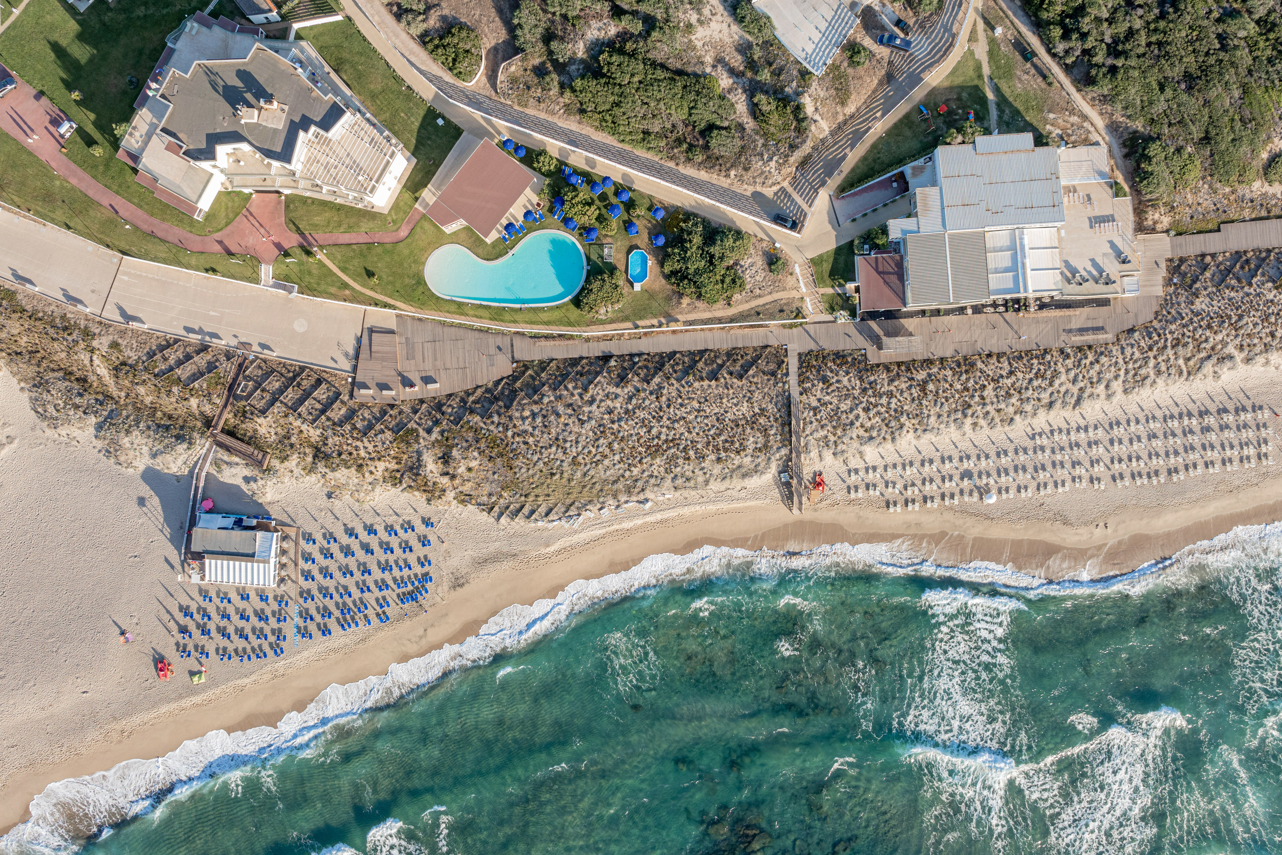 Aerial: coastal resort, sandy beach, ocean, pools, hotel, sun loungers.