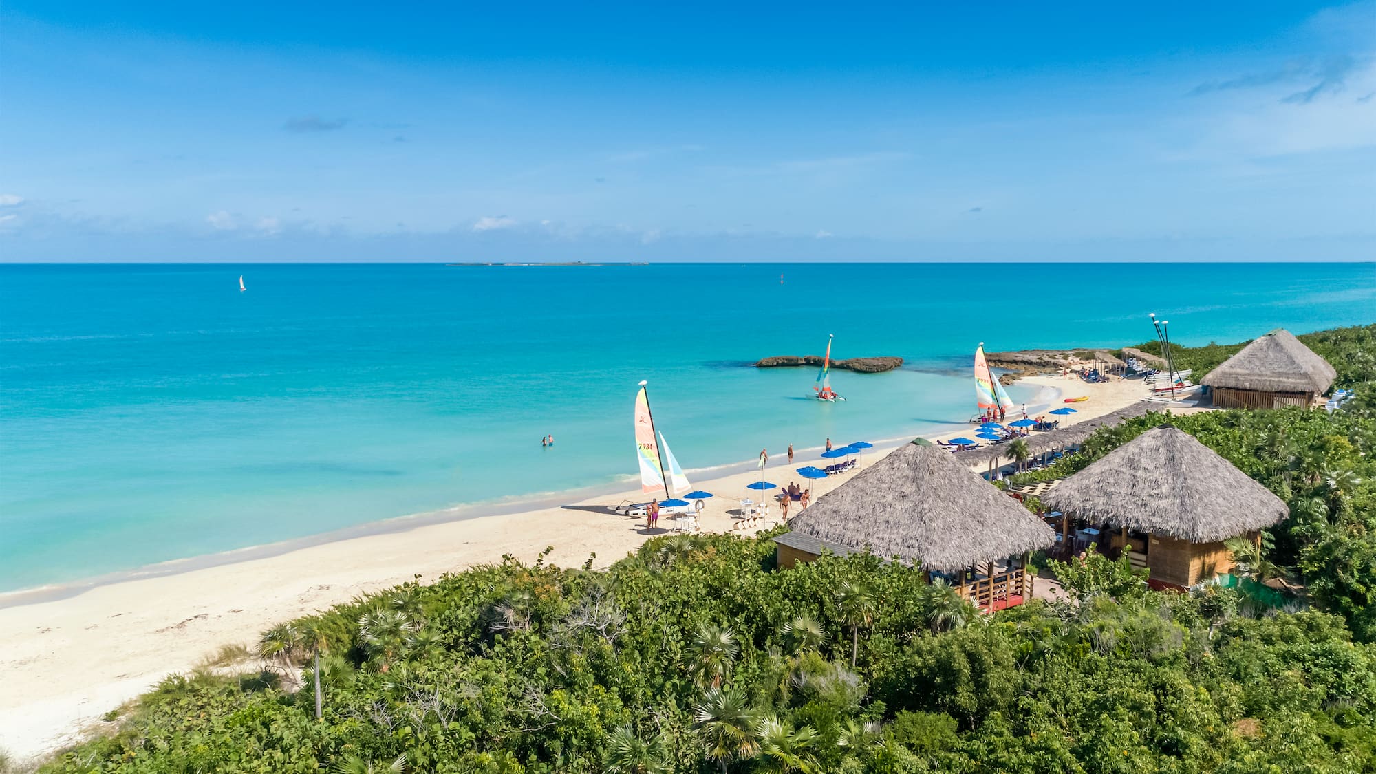 a beach with a group of people and sailboats
