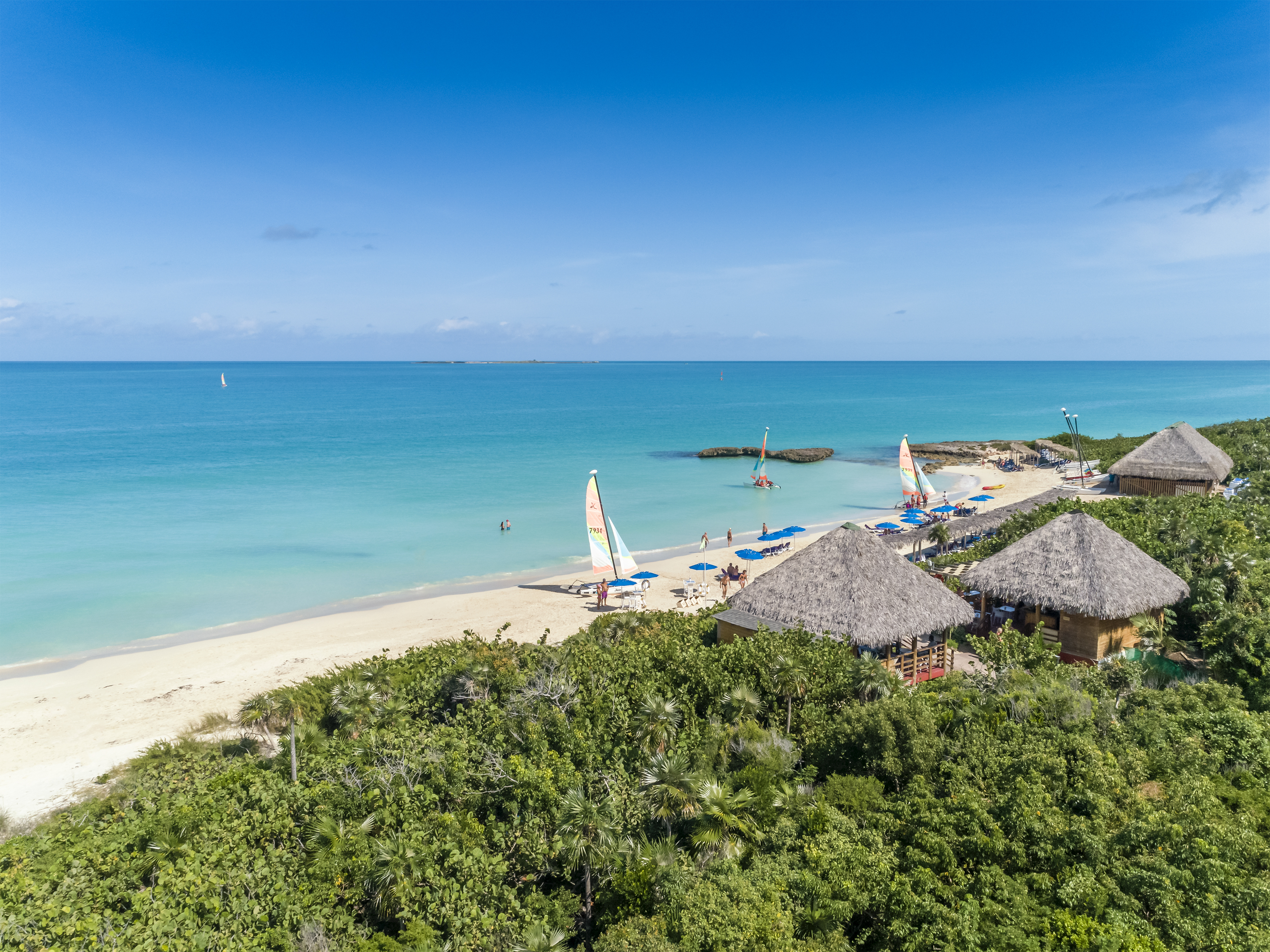 a beach with a group of people and sailboats