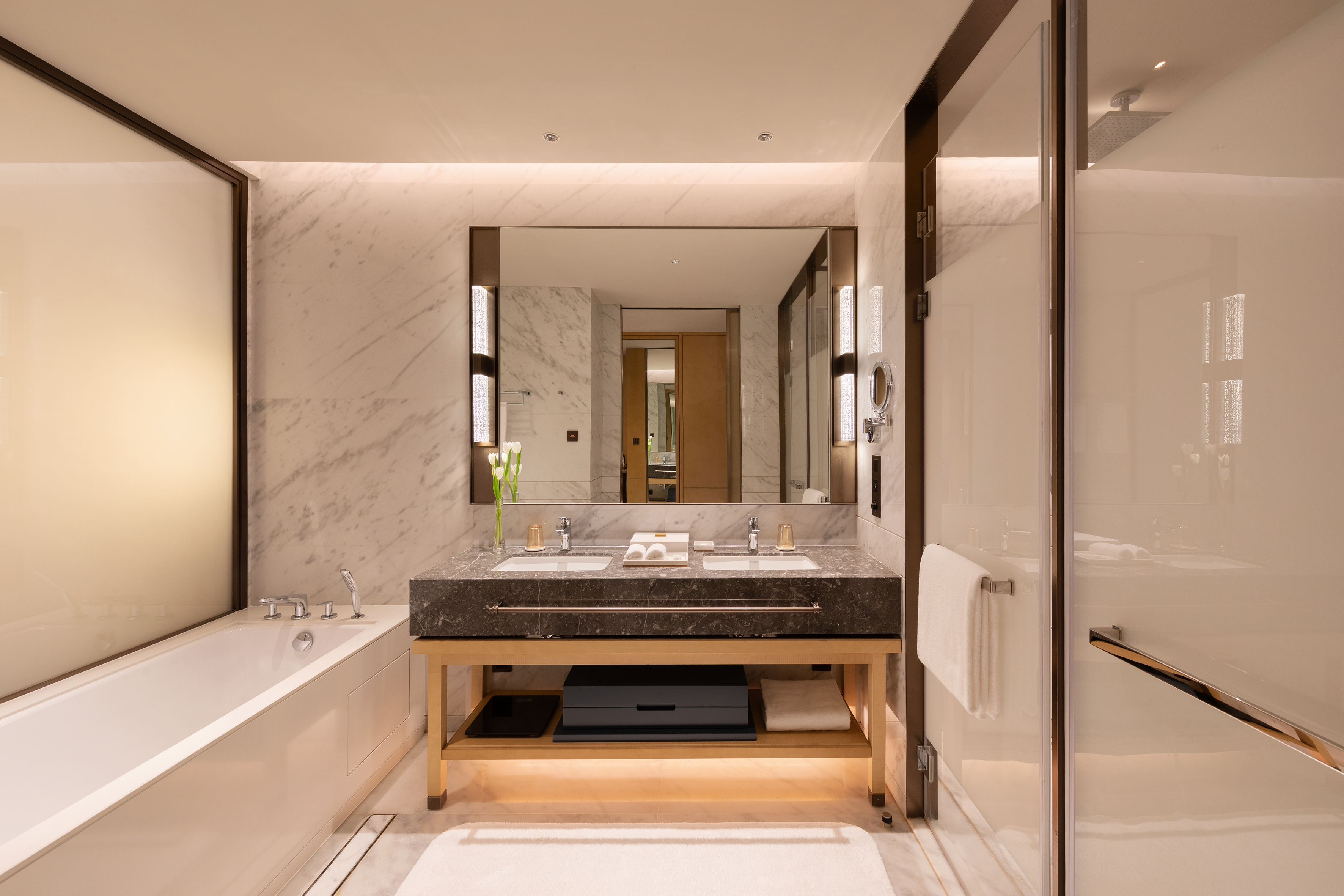 Luxury hotel bathroom with marble double vanity, bathtub, and glass shower.