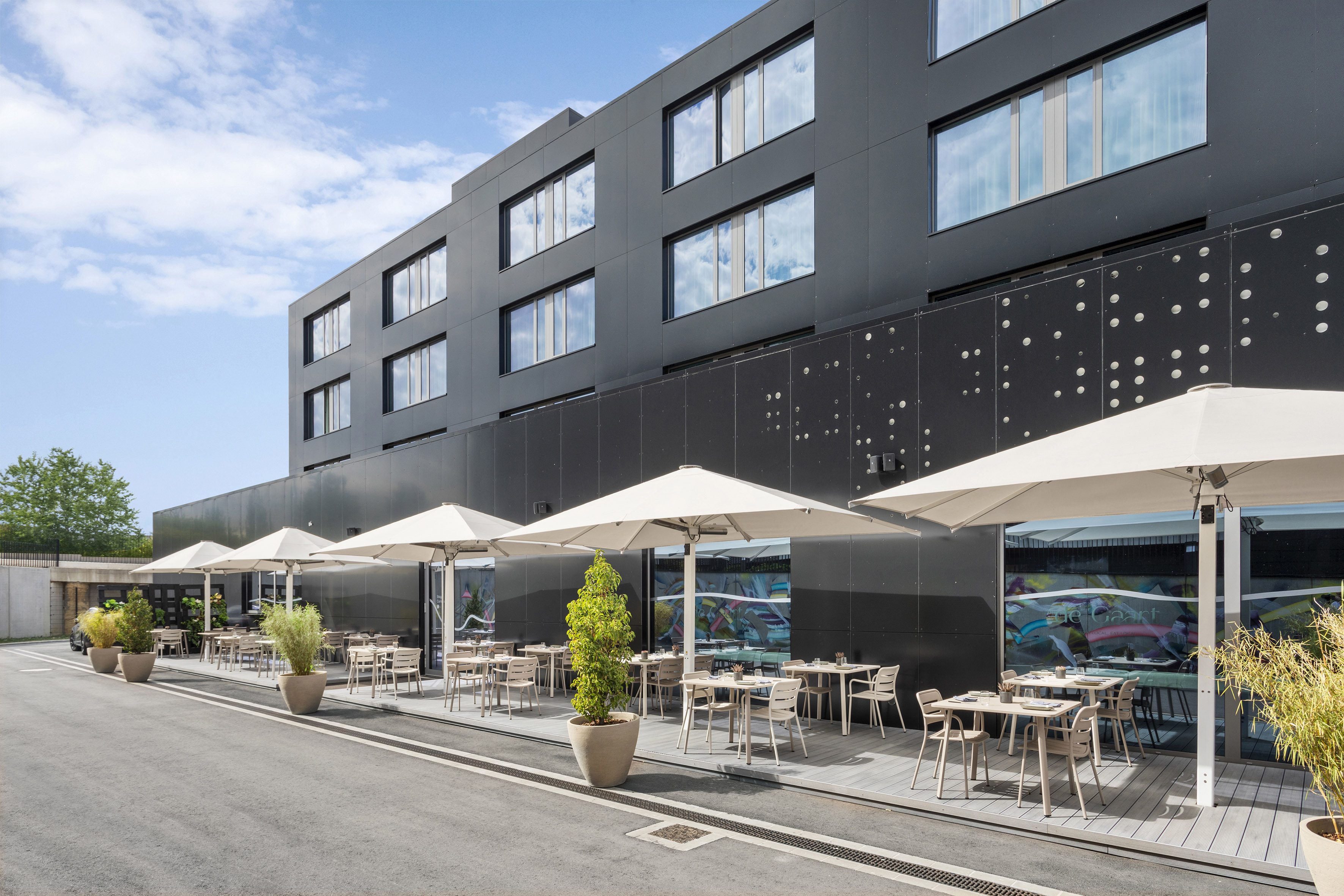 Modern hotel with outdoor dining patio, white umbrellas, and potted greenery. - De Gaart, Cuisine locale - INNSiDE Luxembourg, Luxembourg