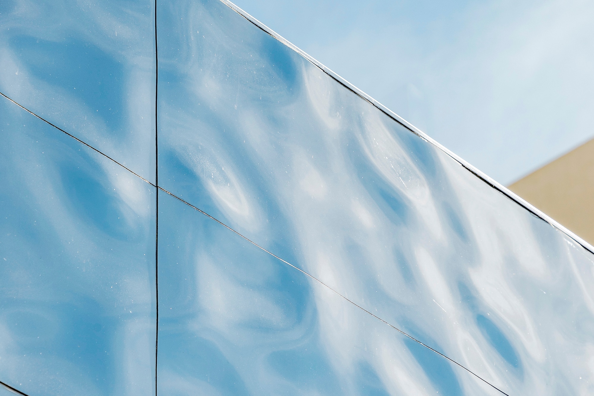 Wavy reflective building facade reflecting a blue sky; modern architecture.