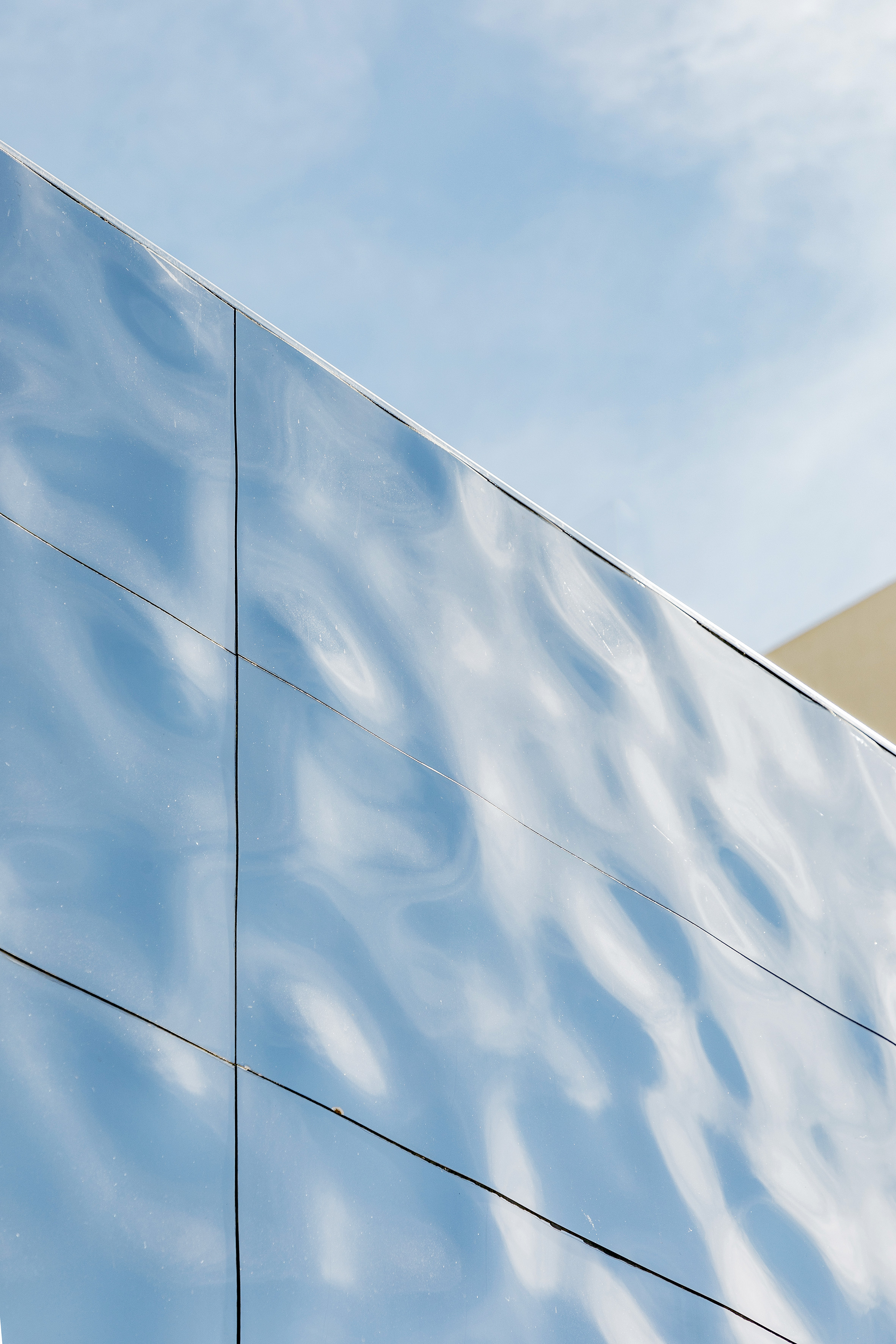 Wavy reflective building facade reflecting a blue sky; modern architecture.