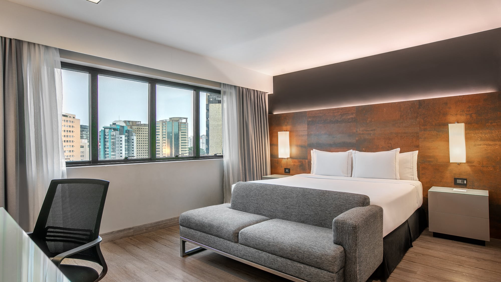 Quarto de hotel moderno com cama de casal, sofá cinza e vista para a cidade. - Deluxe Room Queen - Meliá Ibirapuera, São Paulo