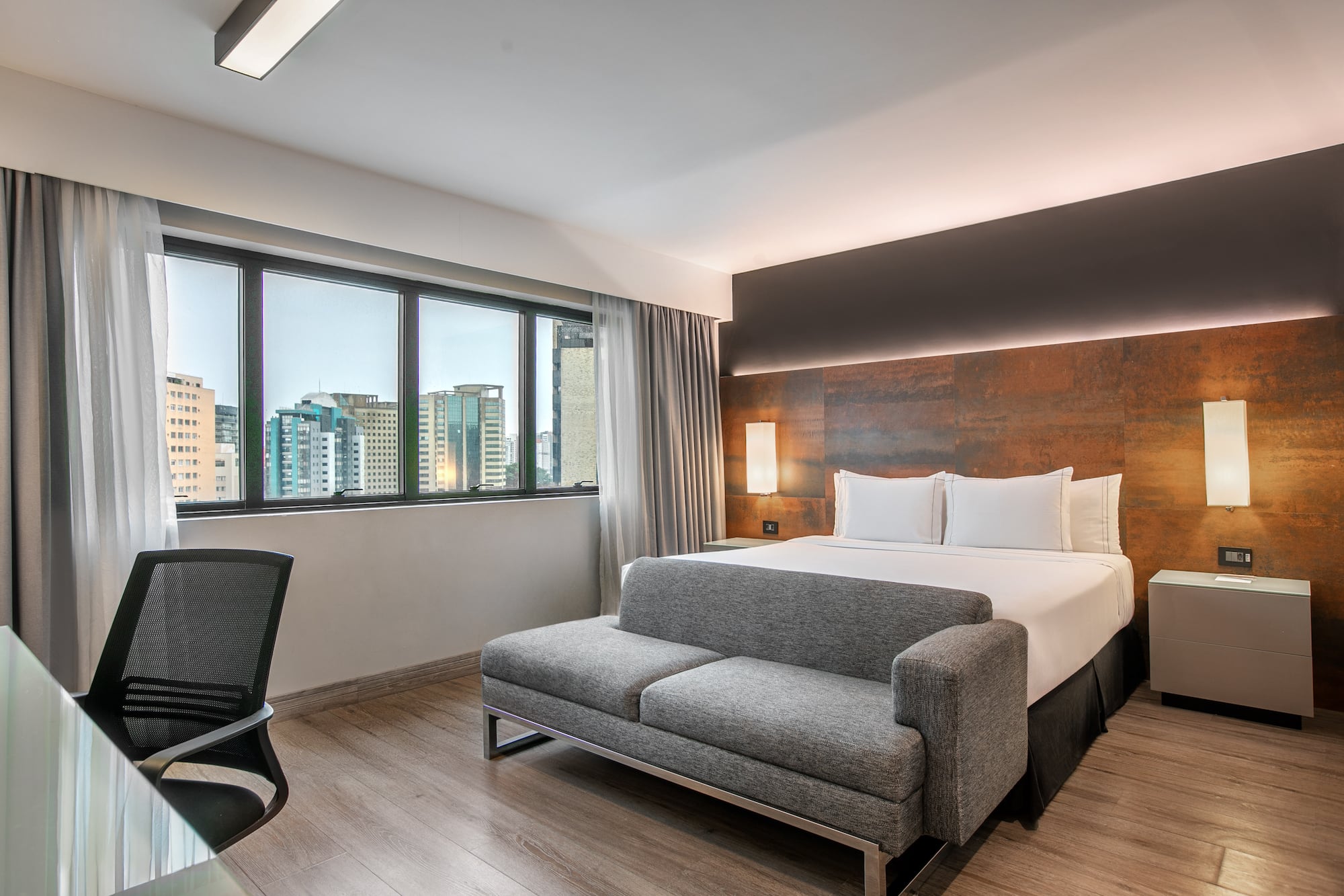 Quarto de hotel moderno com cama de casal, sofá cinza e vista para a cidade. - Deluxe Room Queen - Meliá Ibirapuera, São Paulo