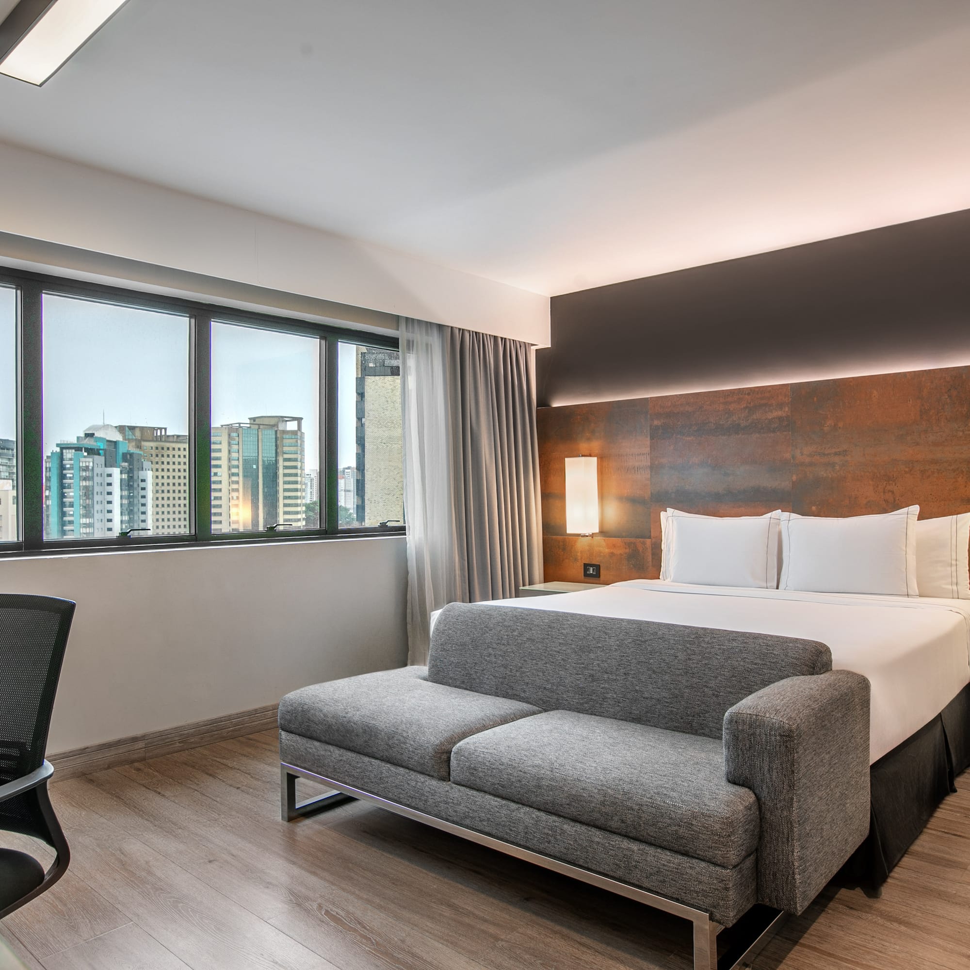 Quarto de hotel moderno com cama de casal, sofá cinza e vista para a cidade. - Deluxe Room Queen - Meliá Ibirapuera, São Paulo