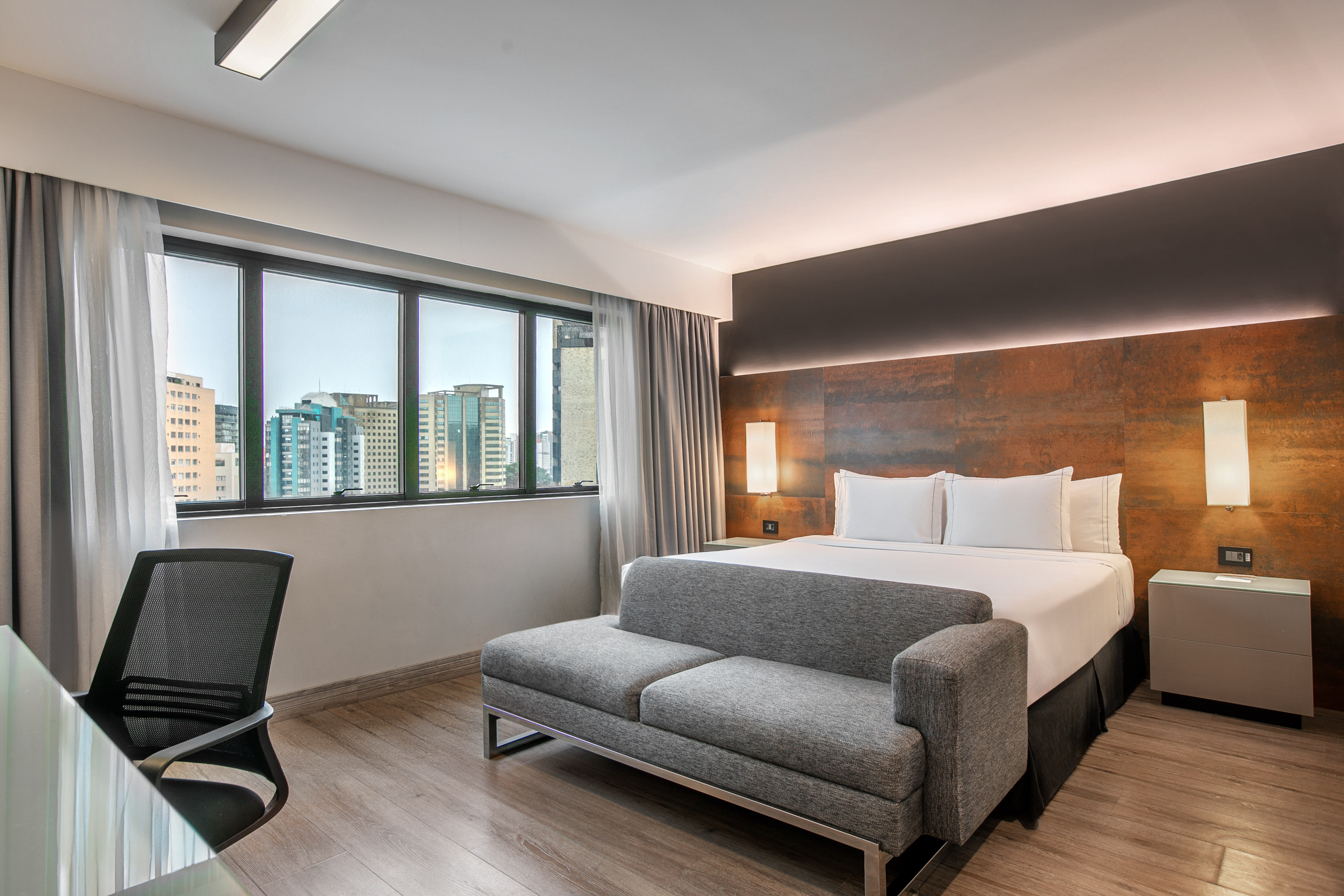 Quarto de hotel moderno com cama de casal, sofá cinza e vista para a cidade. - Deluxe Room Queen - Meliá Ibirapuera, São Paulo