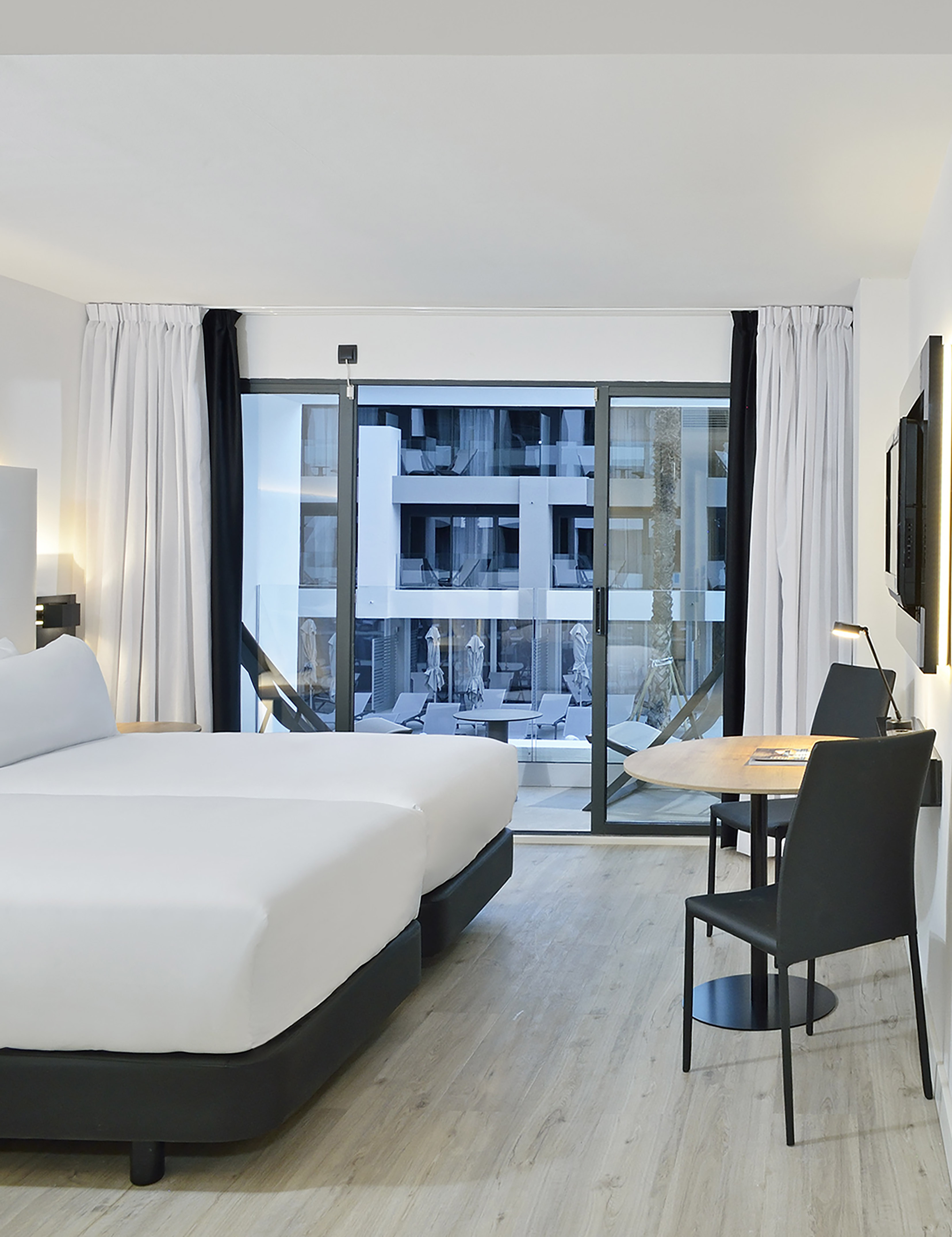 Modern hotel room with twin beds, dining table, and balcony with resort view.