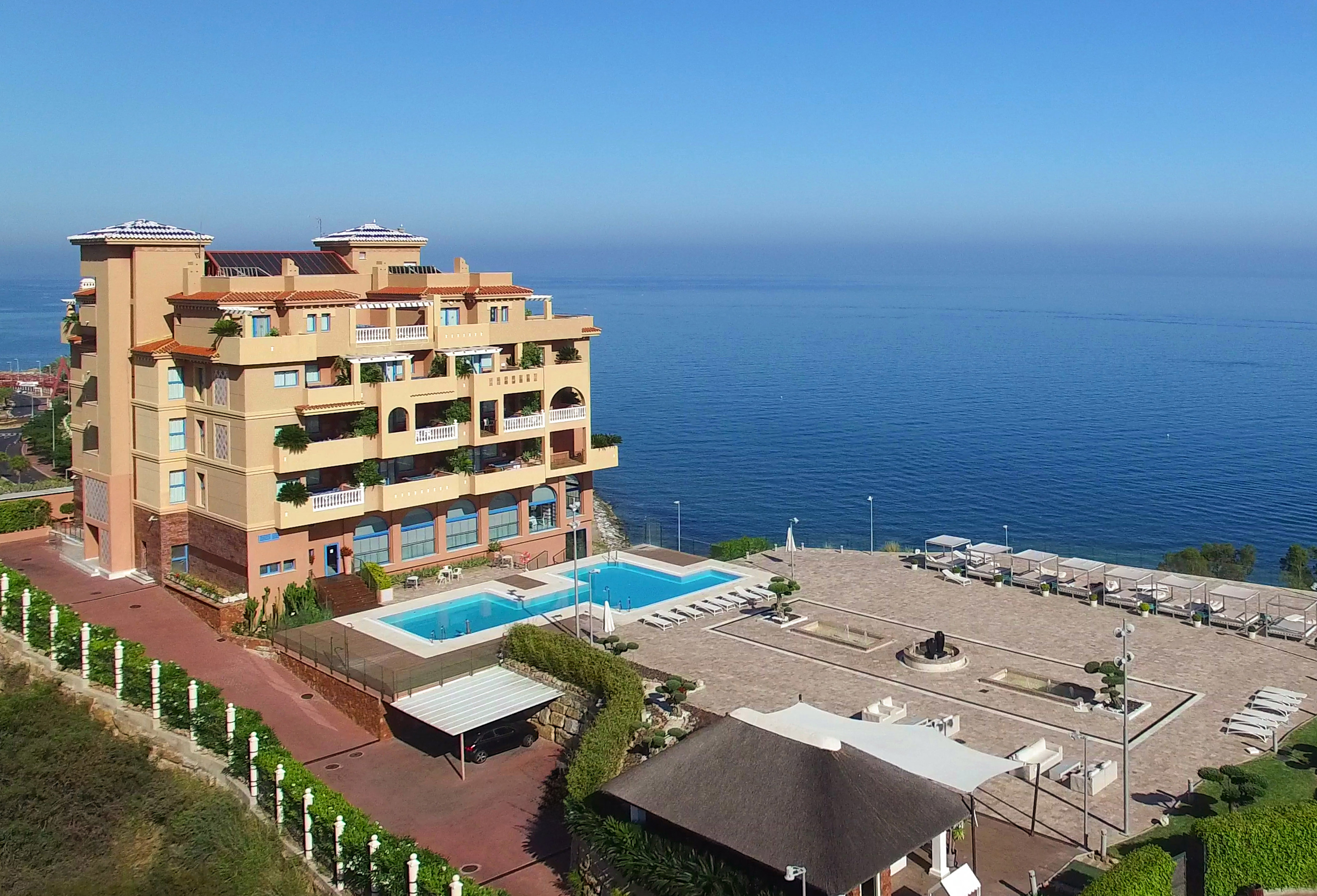 Luxury coastal resort with ocean view, two swimming pools, and sunbeds.