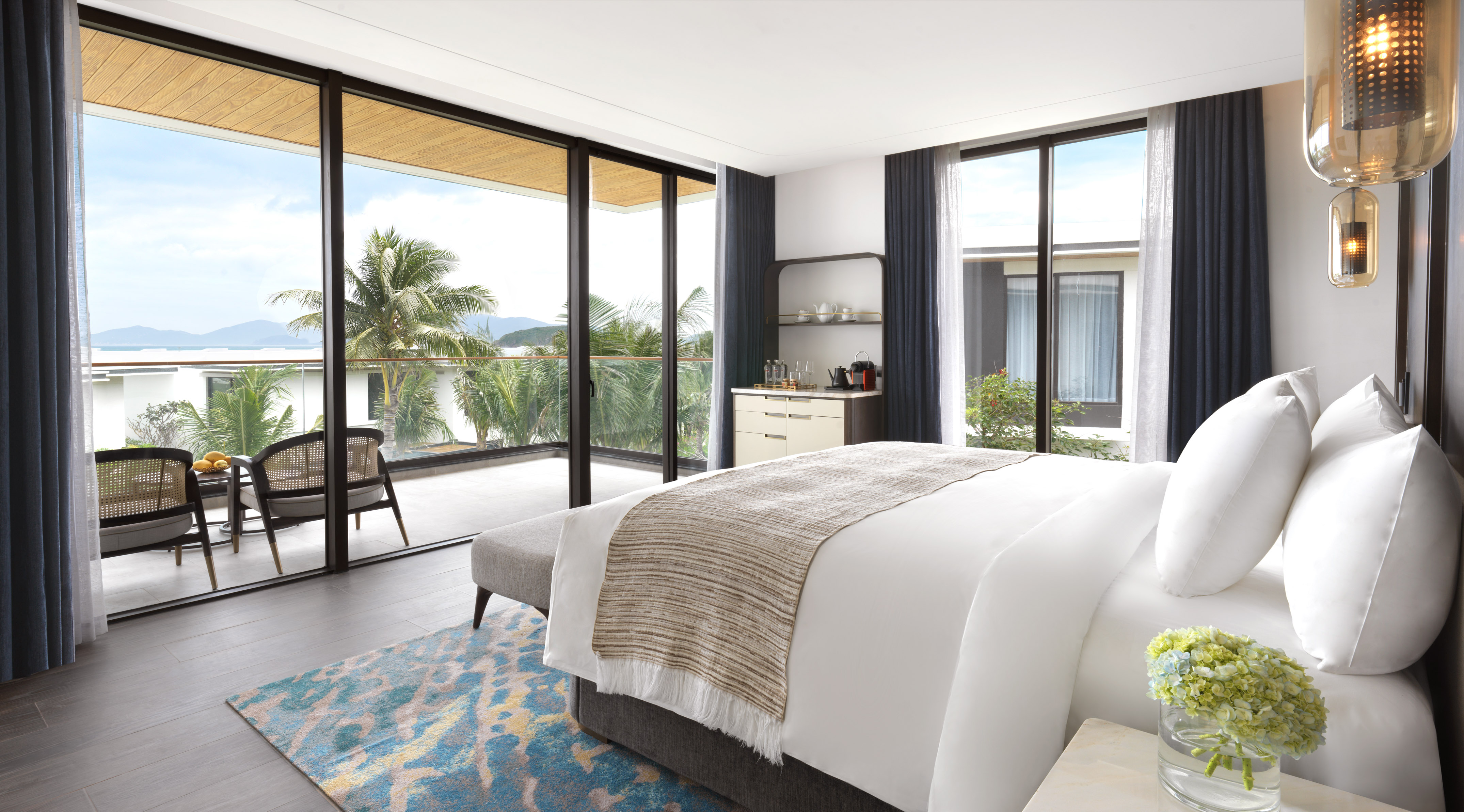 Modern hotel bedroom with ocean view balcony, tropical landscape.
