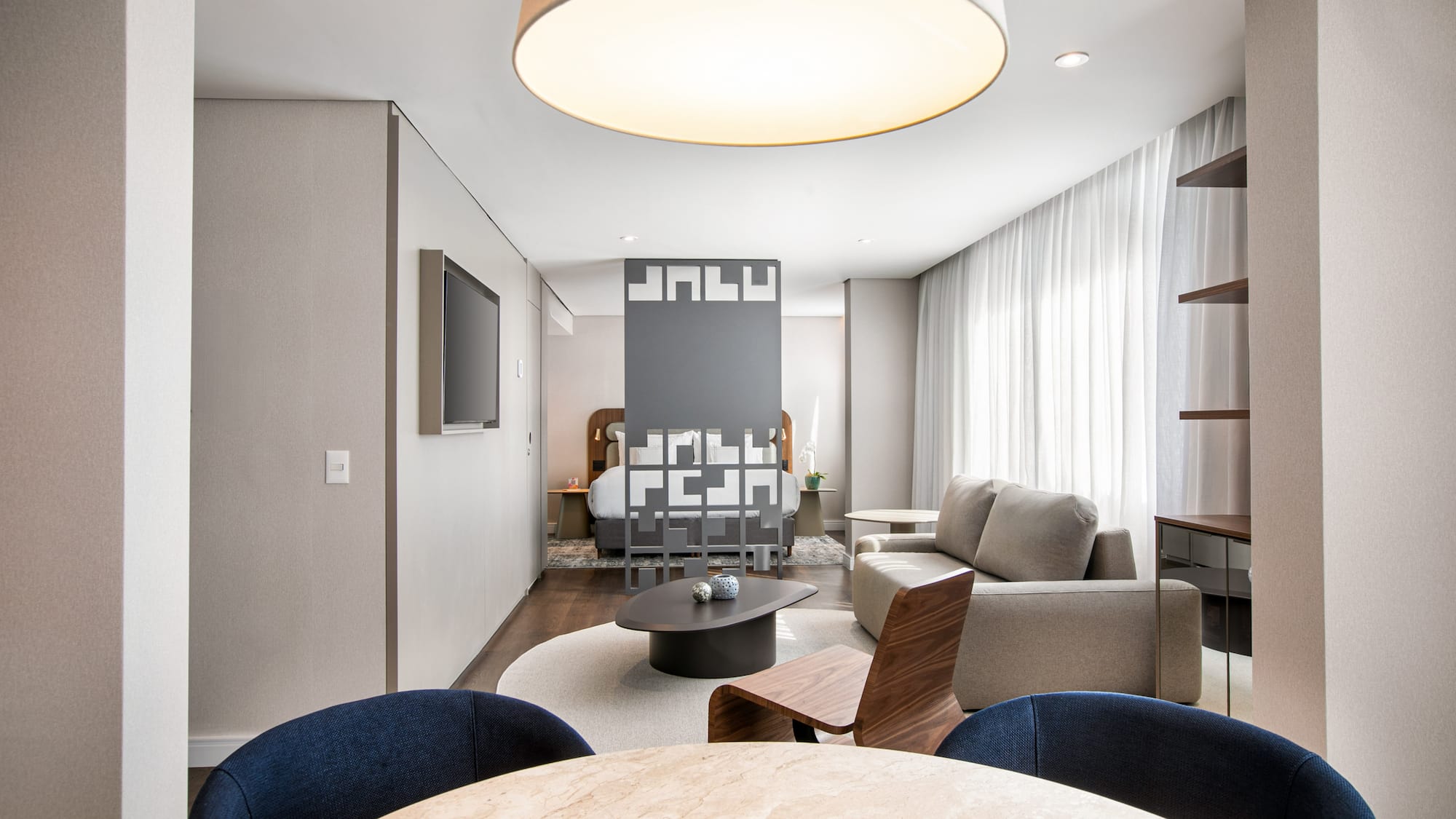 Modern hotel suite with open-plan living room, bedroom, and dining space.