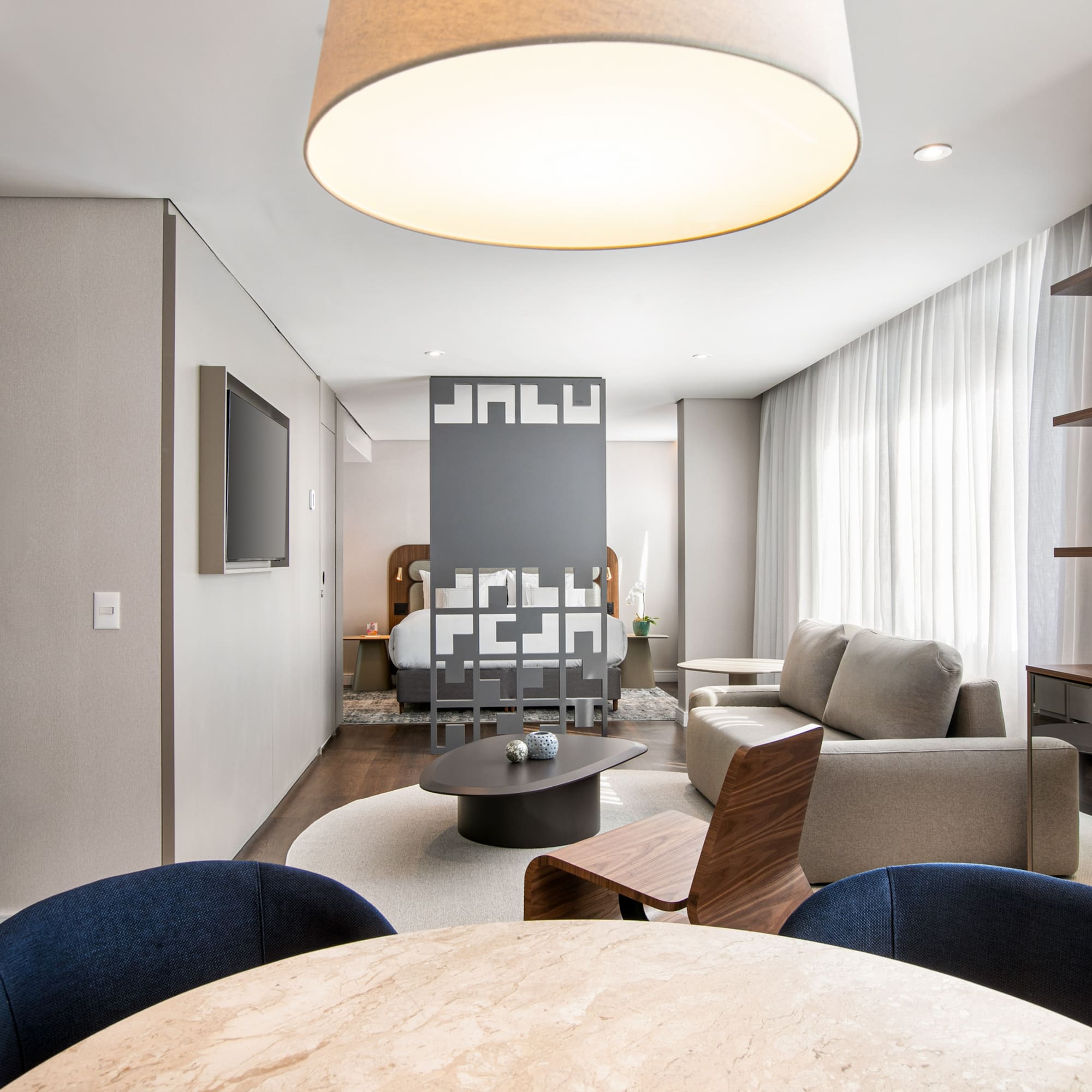 Modern hotel suite with open-plan living room, bedroom, and dining space.
