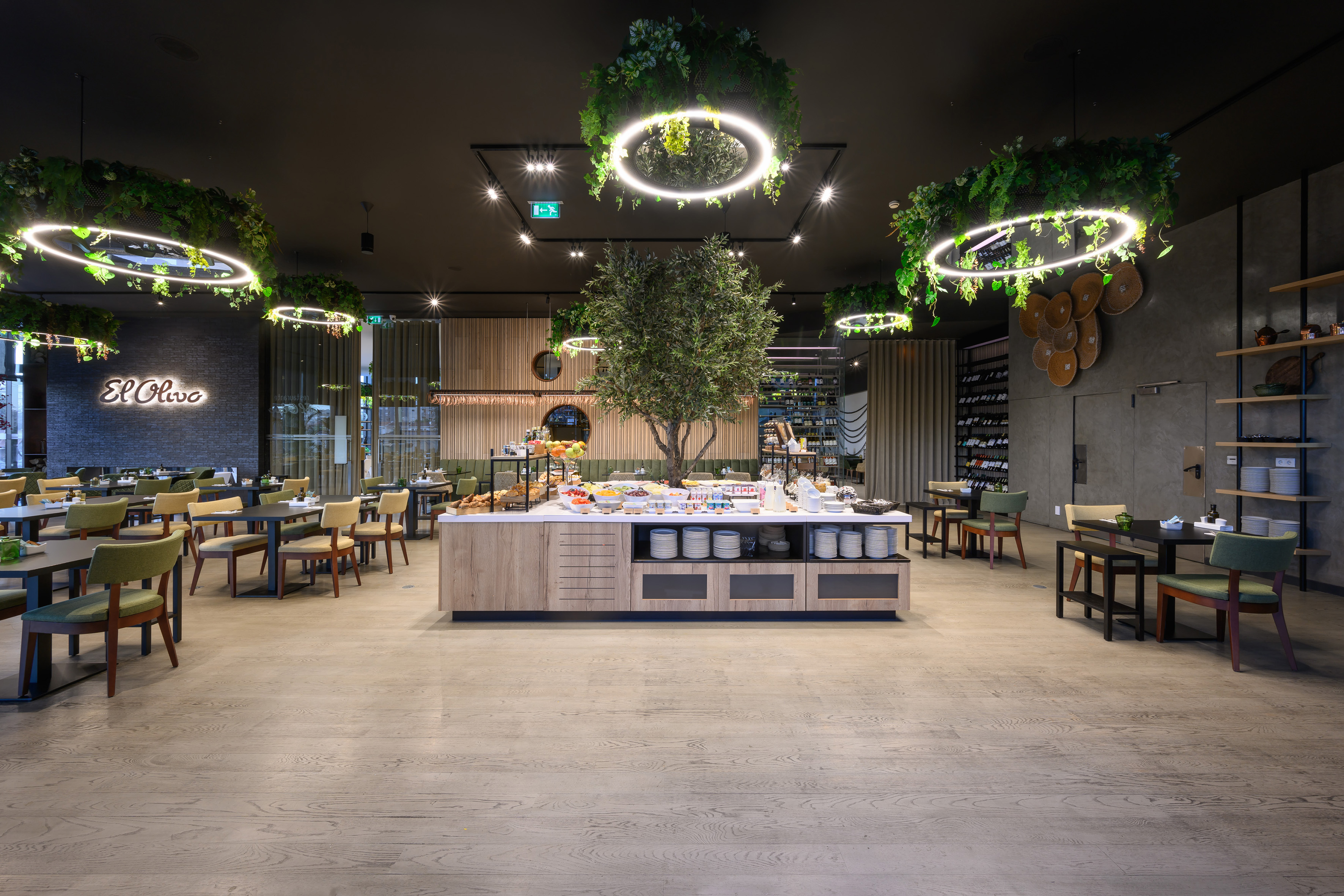 Restaurant buffet with olive tree centerpiece and modern illuminated decor.