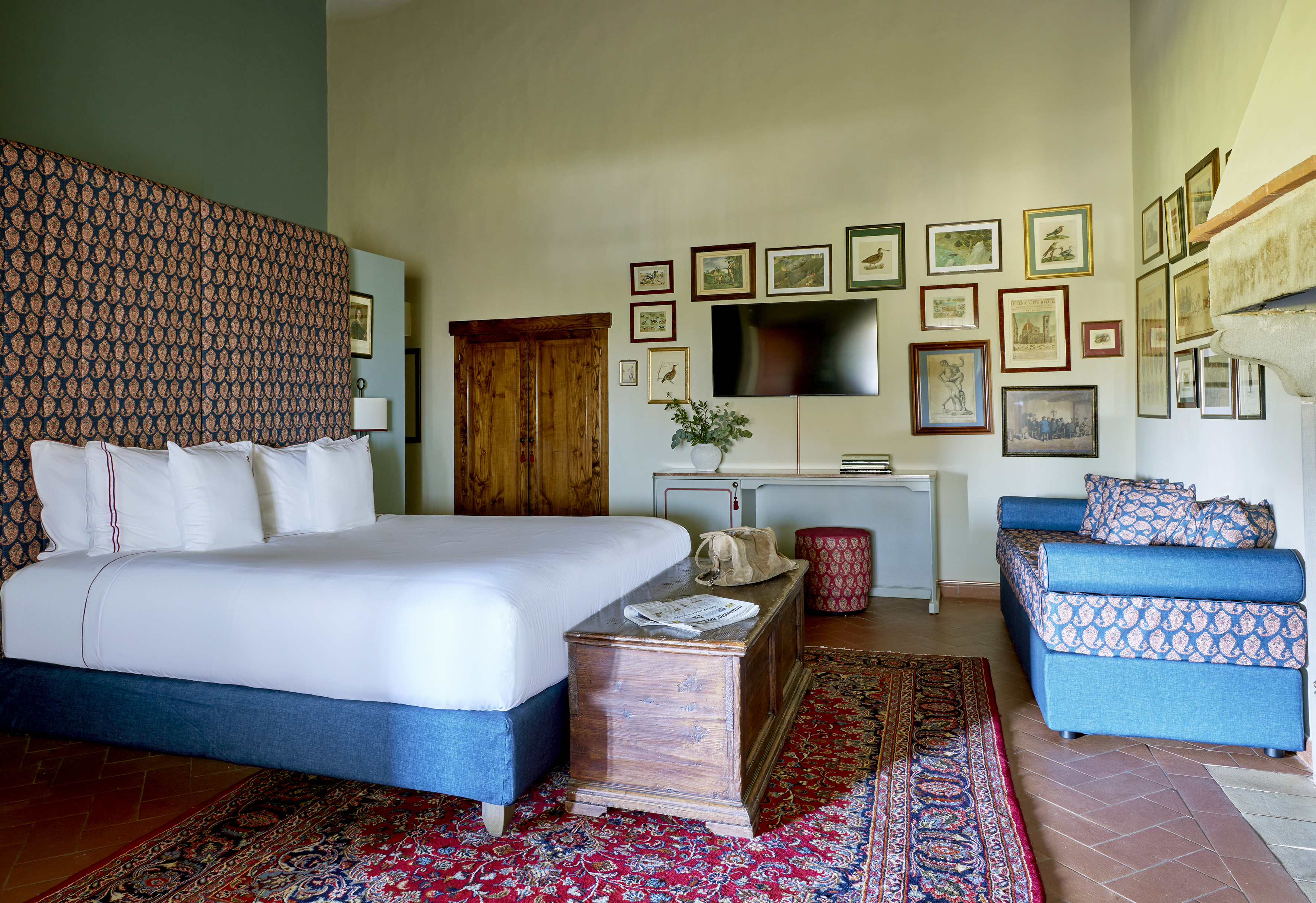 Traditional bedroom with patterned bed, red rug, blue daybed, and framed art.