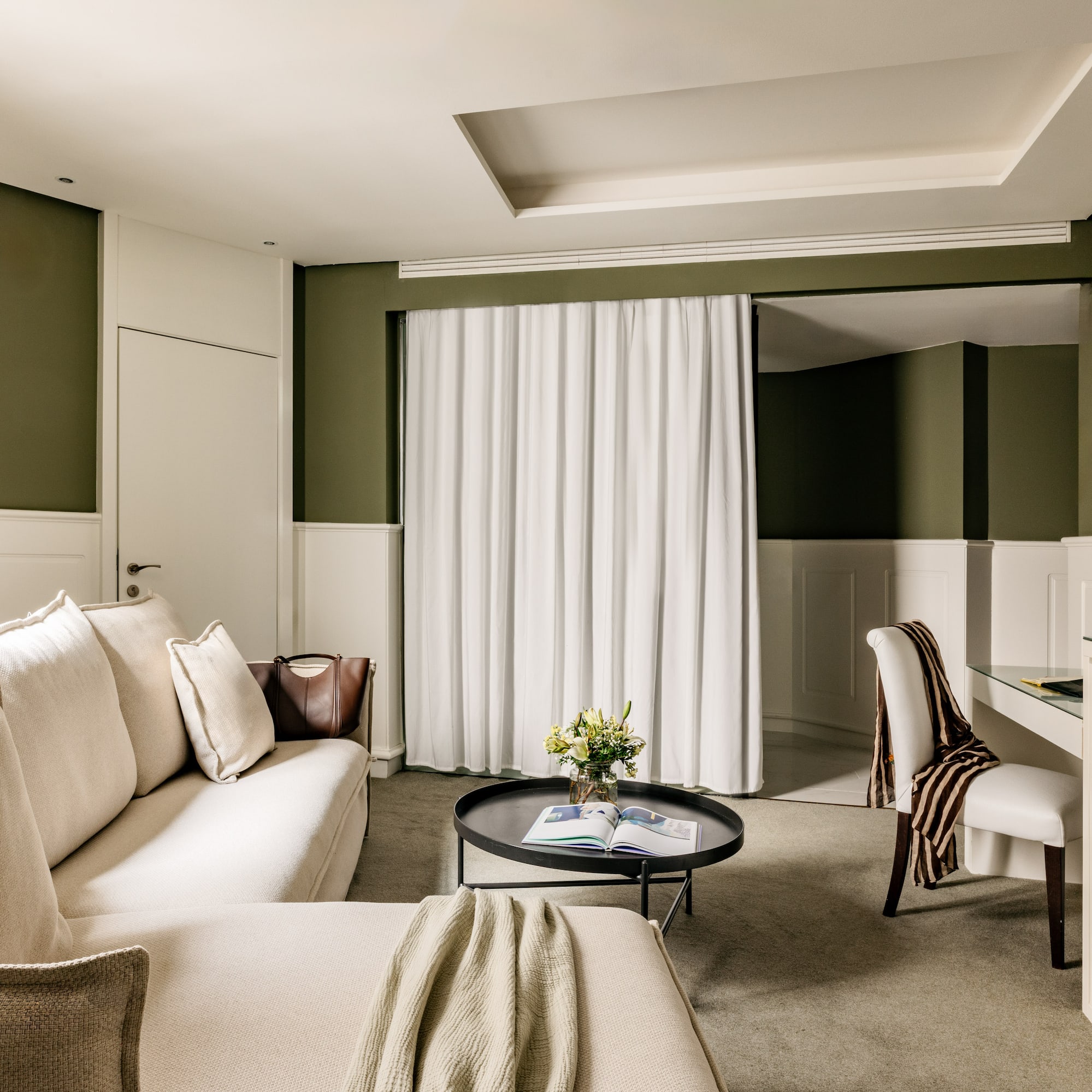 Suite de hotel elegante con sofá beige, mesa centro, paredes verde oliva.