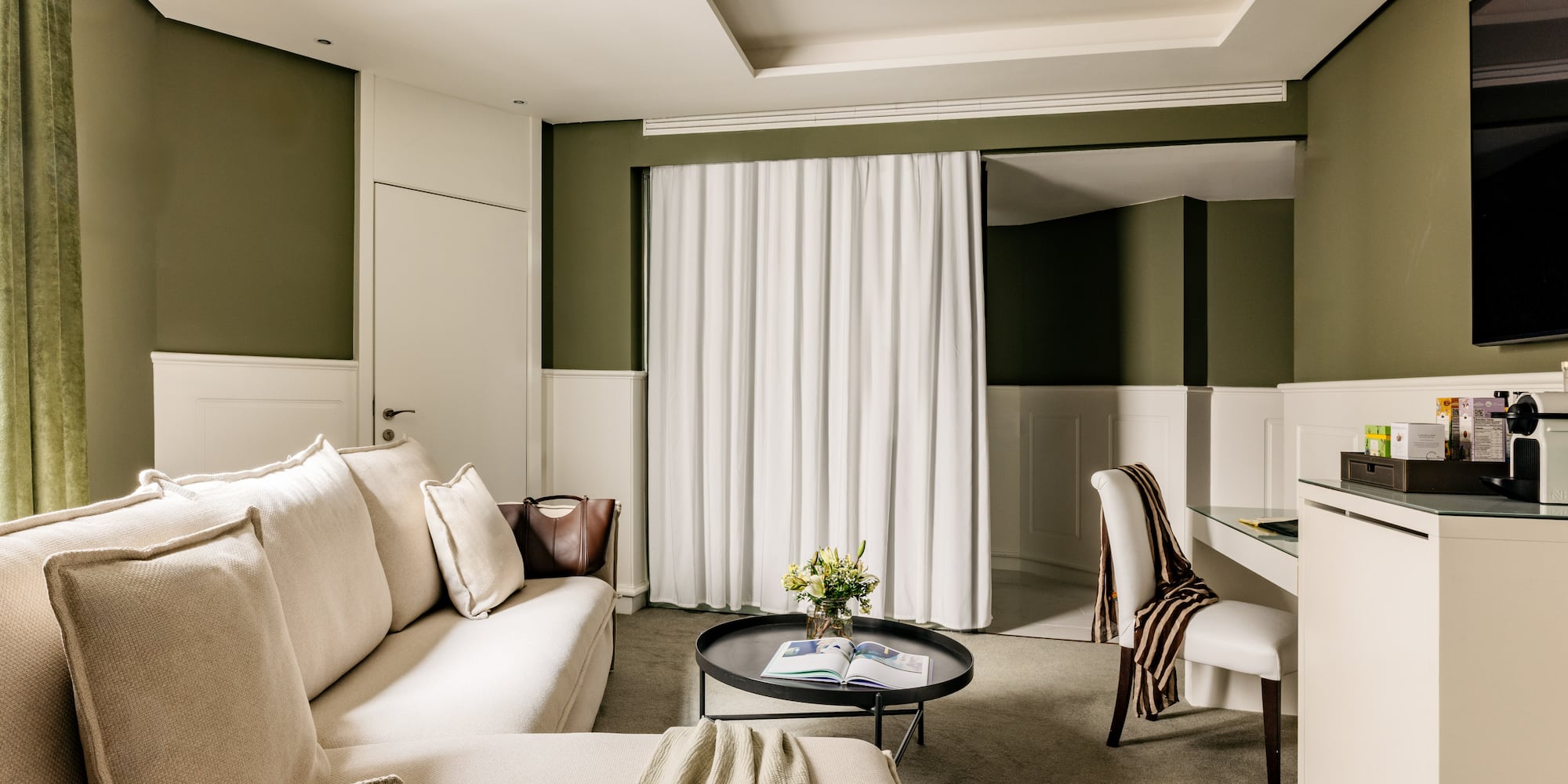 Suite de hotel elegante con sofá beige, mesa centro, paredes verde oliva.