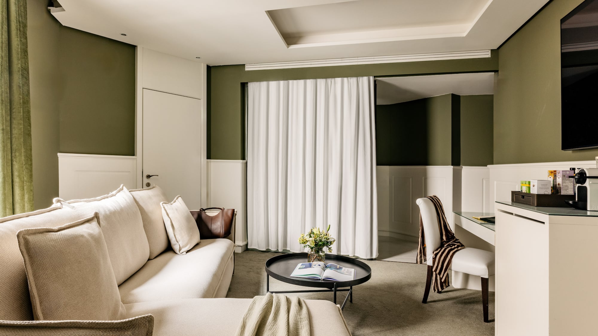 Suite de hotel elegante con sofá beige, mesa centro, paredes verde oliva.