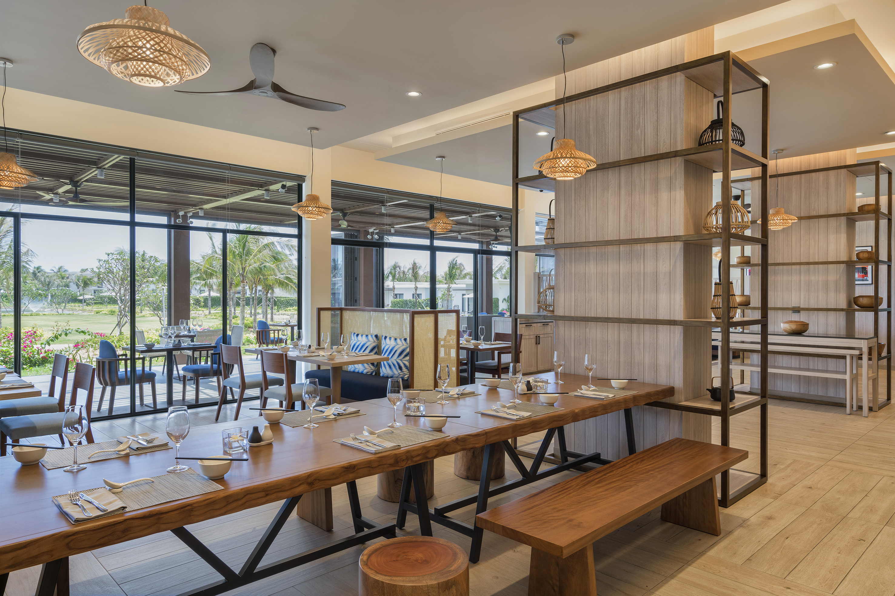 Modern resort restaurant with wooden tables, woven lights, and tropical views.
