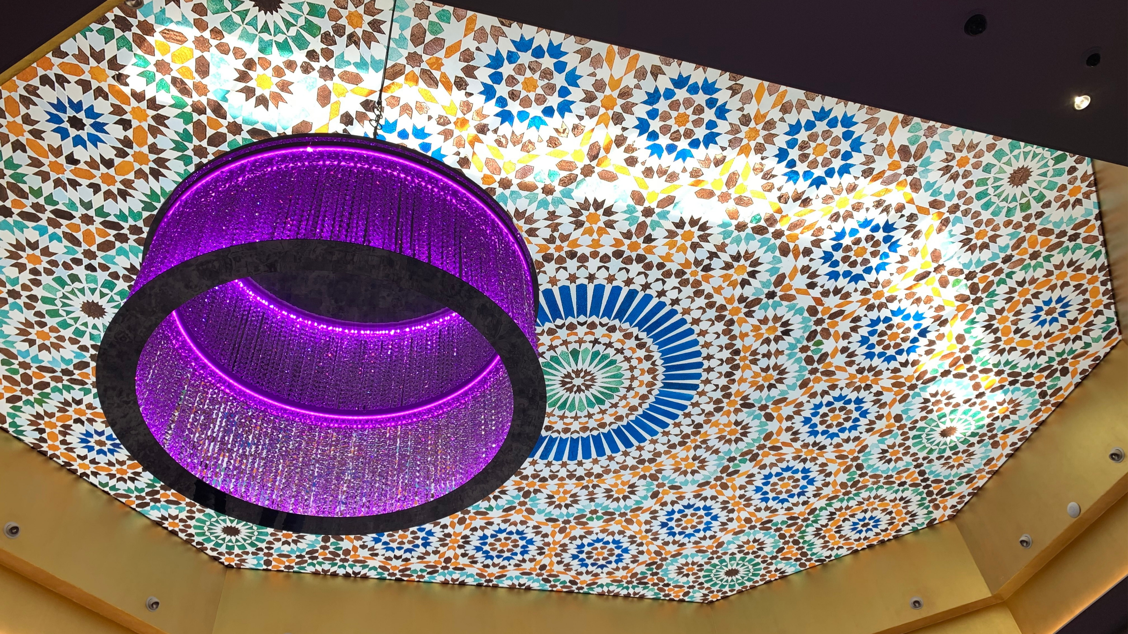 Purple crystal chandelier, colorful Moroccan geometric ceiling.